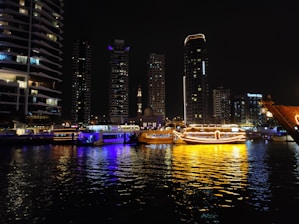 City skyline with illuminated boats on the water at night.