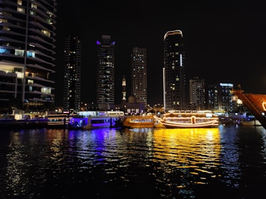 City skyline with illuminated boats on the water at night.
