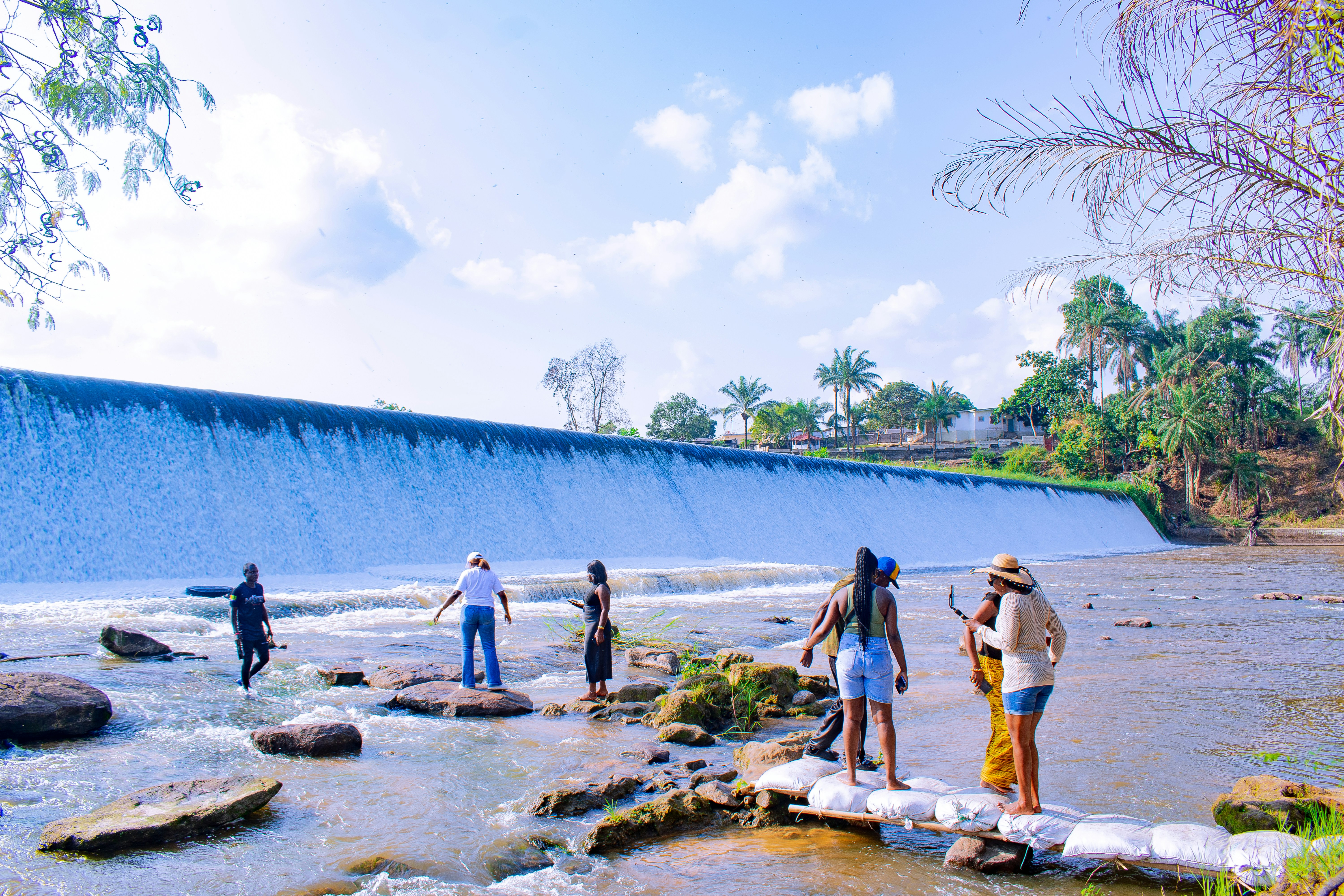 People standing near a wide waterfall on a sunny day