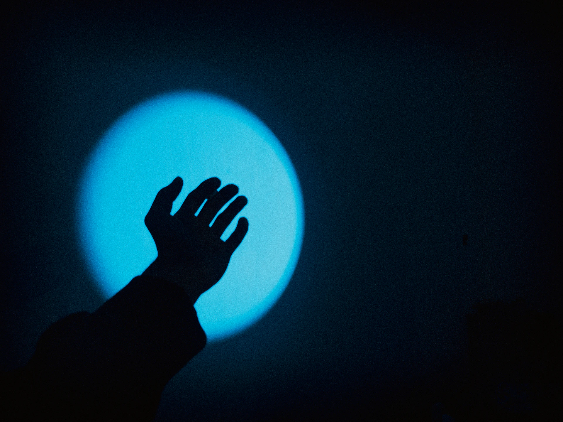 Silhouette of a hand reaching towards a blue light