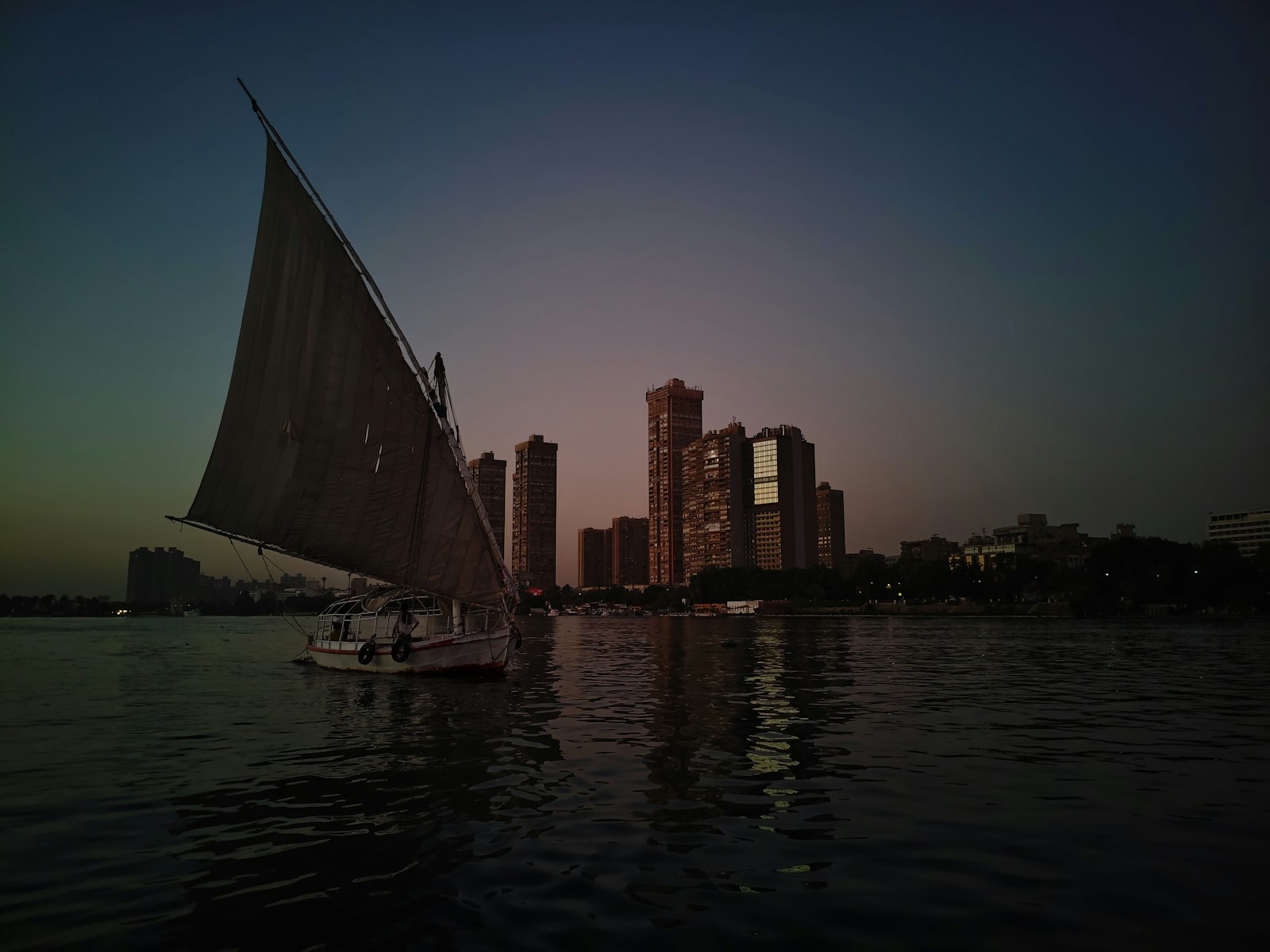 A traditional felucca sailing the Nile with the Cairo skyline at dusk