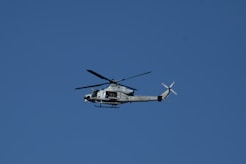 A military helicopter flies against a clear blue sky.