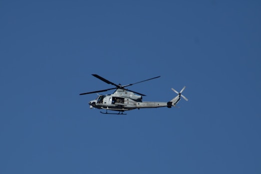 A military helicopter flies against a clear blue sky.