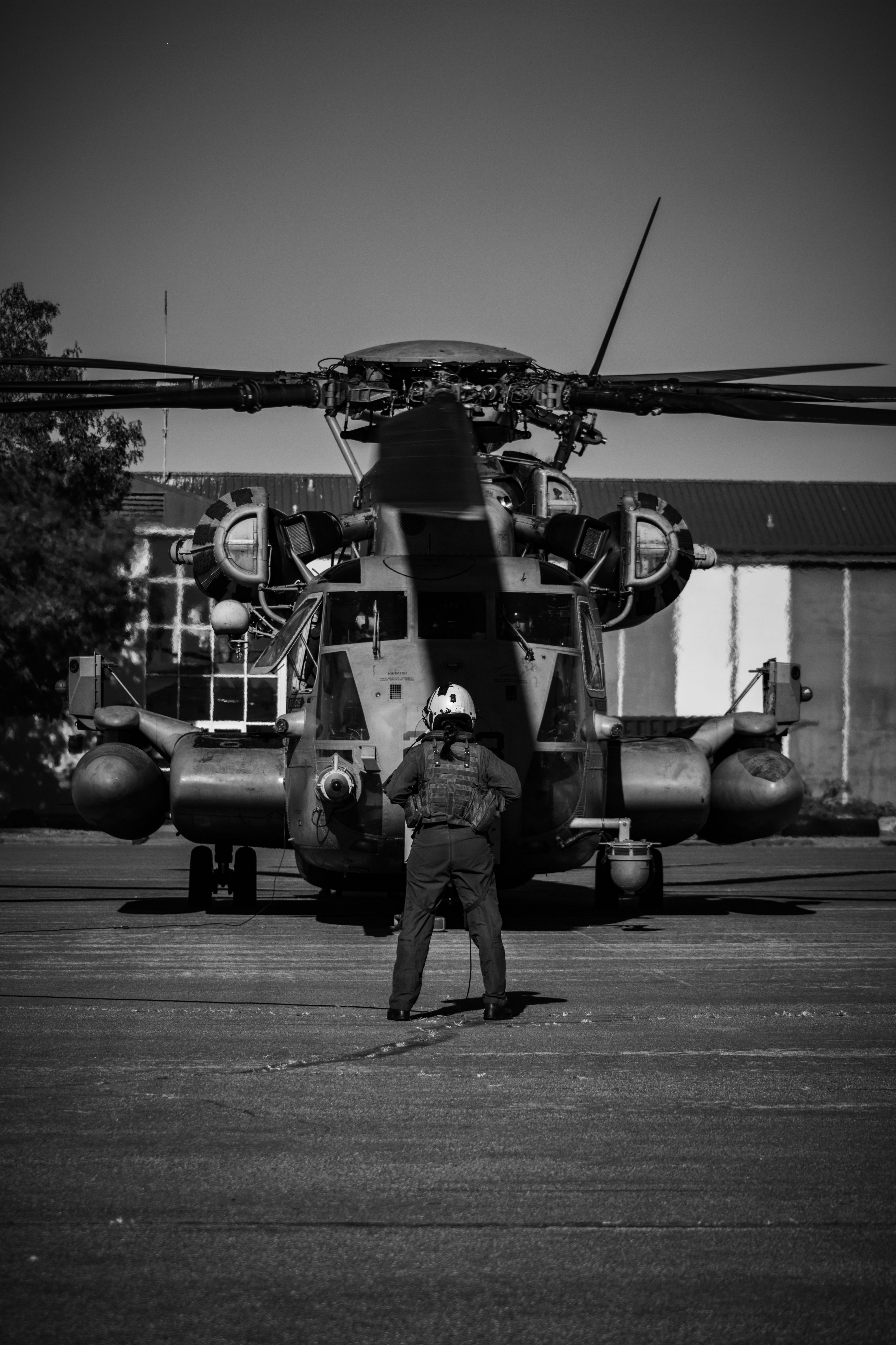Pilot stands before a large military helicopter on tarmac.