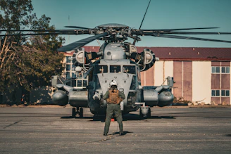 Pilot stands before a large military helicopter on tarmac