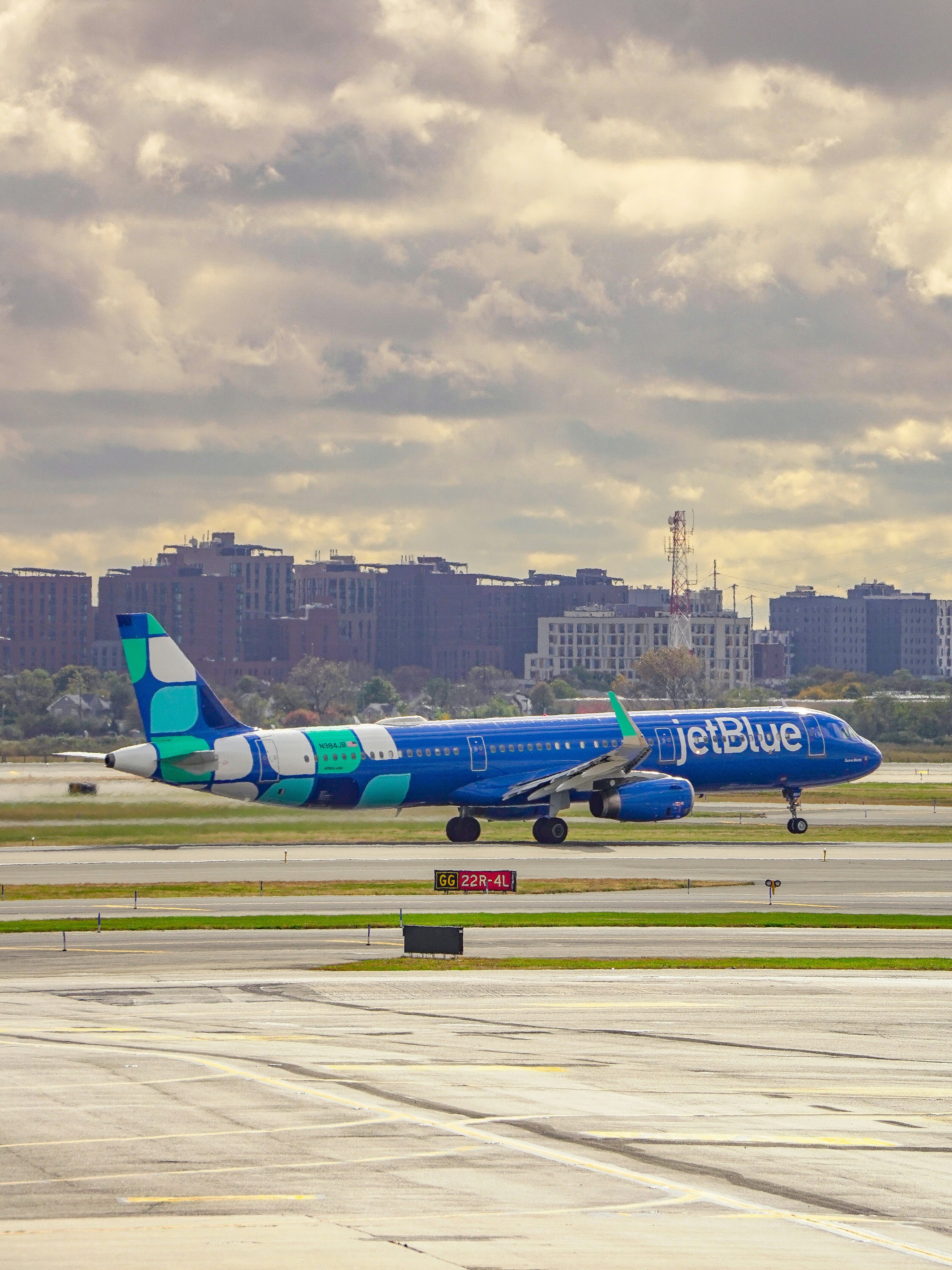 Jetblue airplane taxiing on the runway with buildings behind.