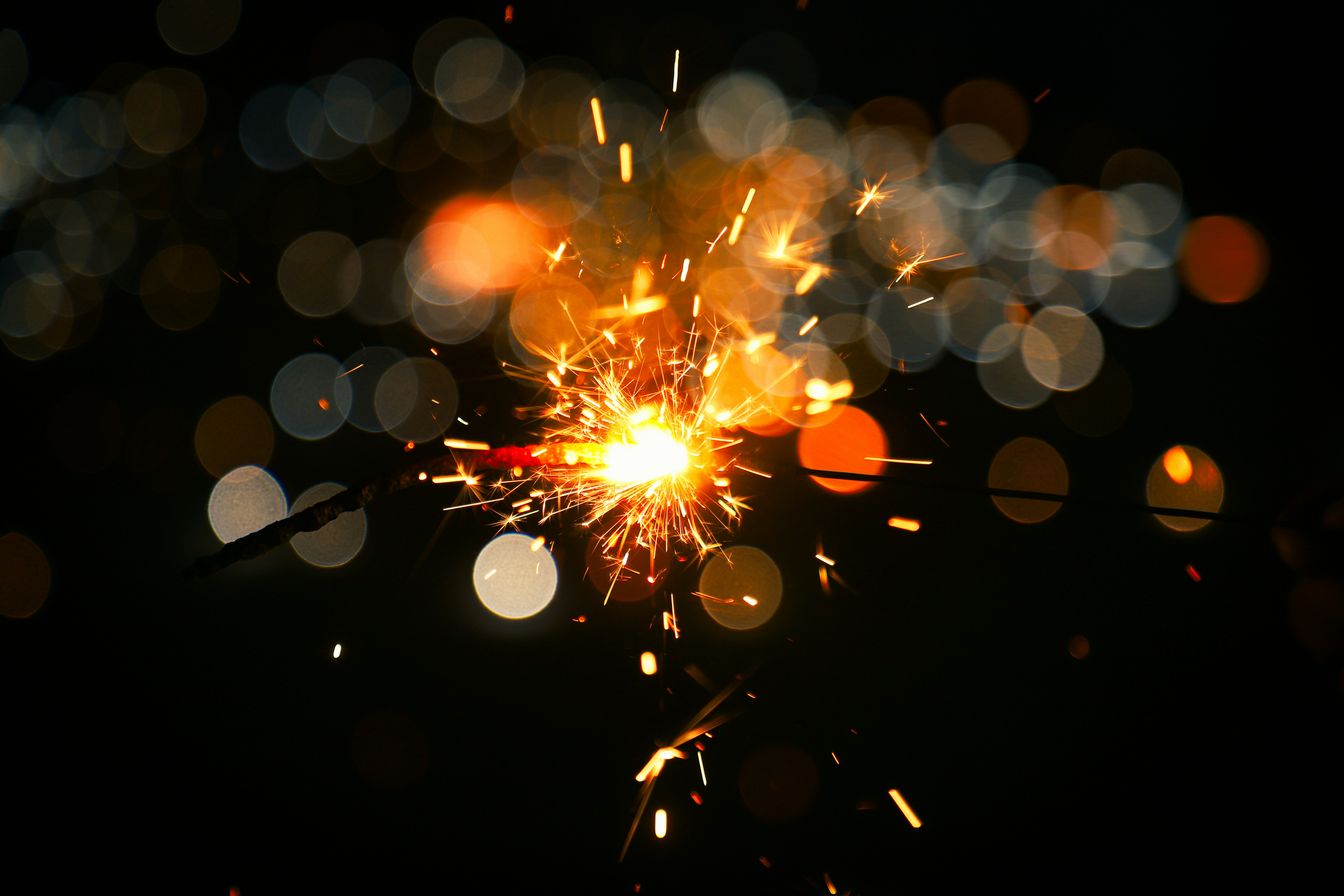 Sparkler ignites with bright orange sparks against bokeh lights.