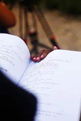 Hand resting on open script with camera in background.
