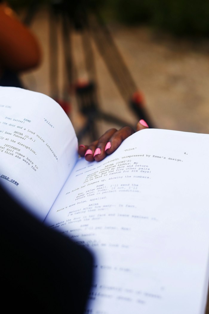 A hand resting on an open script with a camera behind it