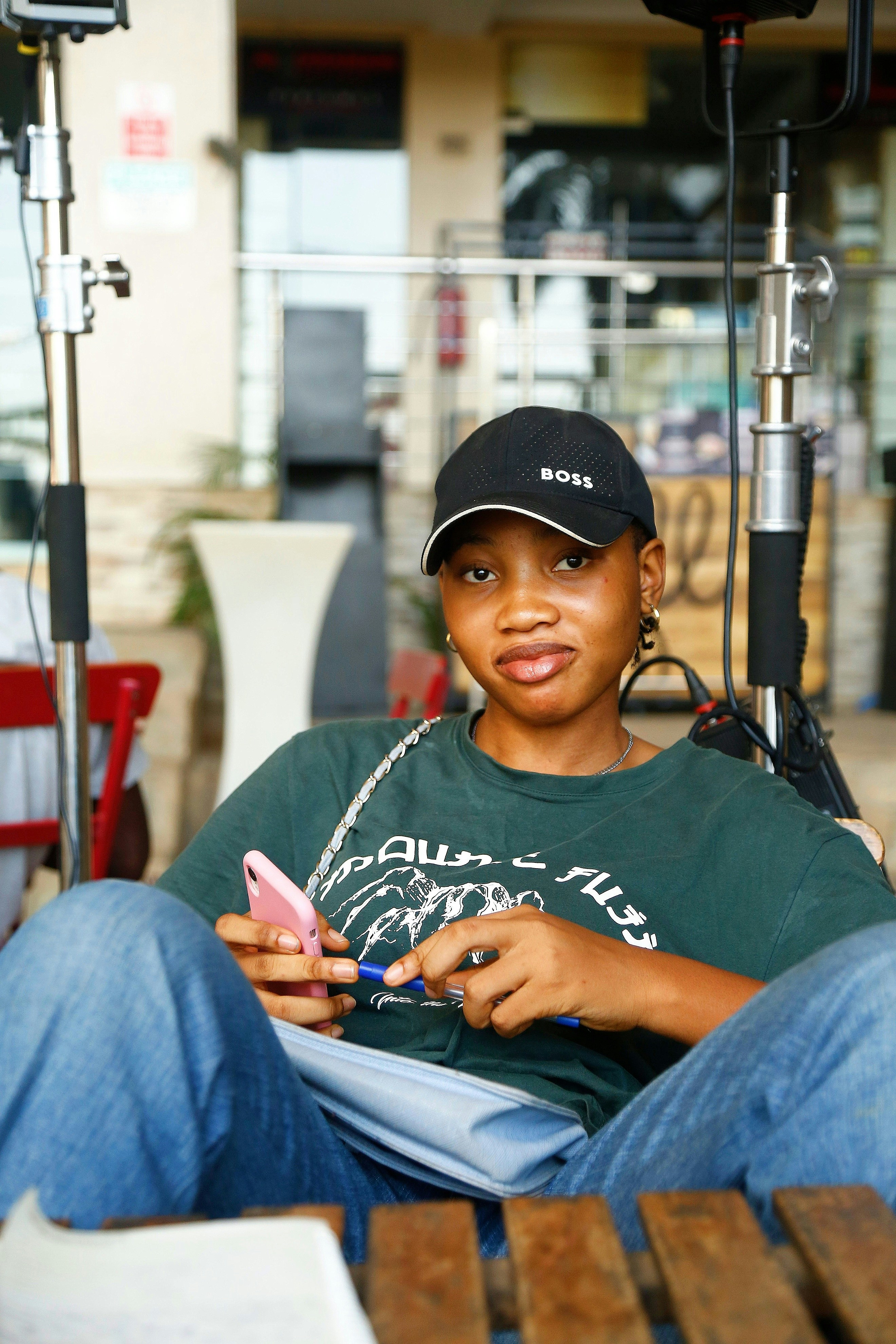 Young woman in baseball cap holding phone and pen.