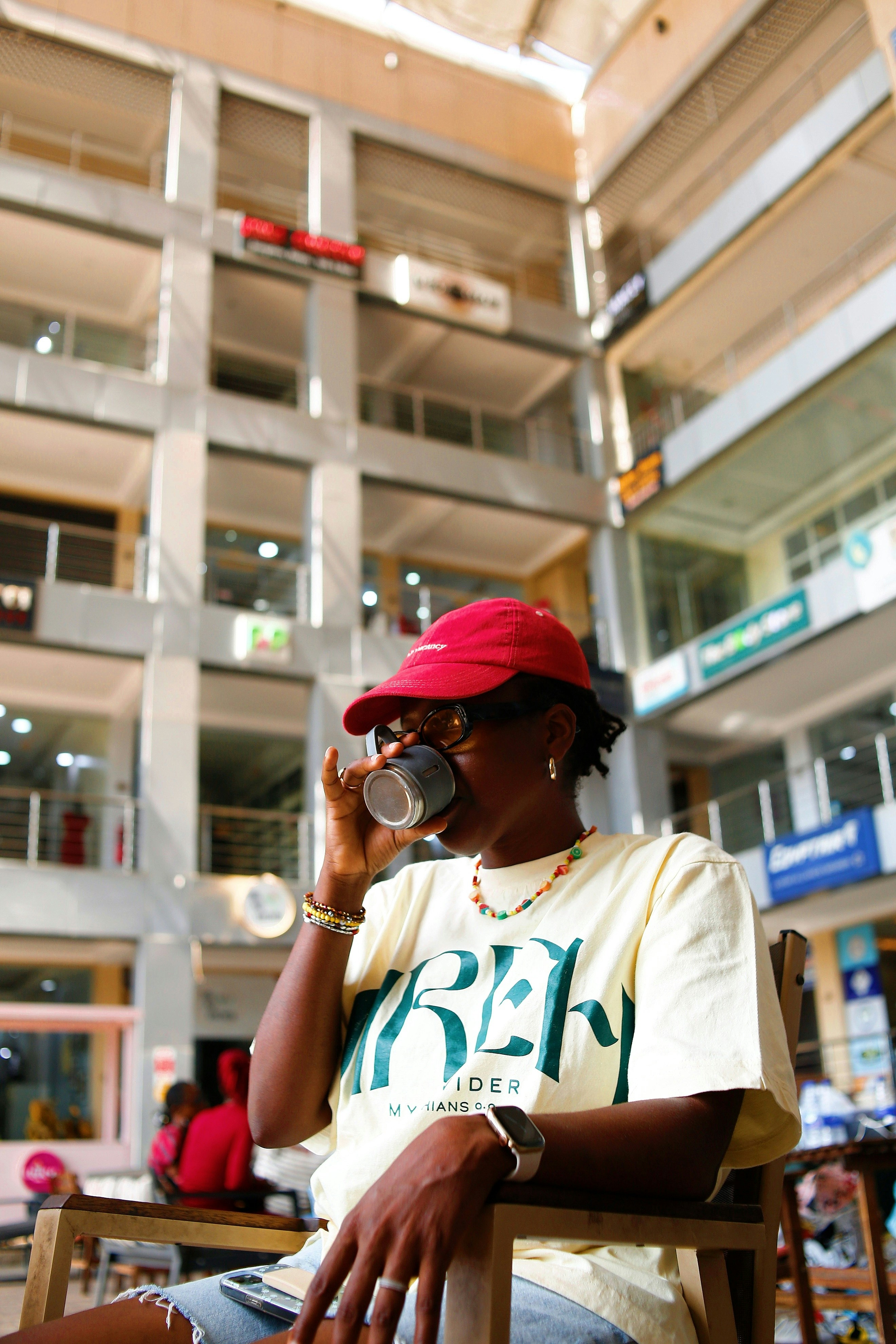 Woman in red hat drinks from cup in building atrium