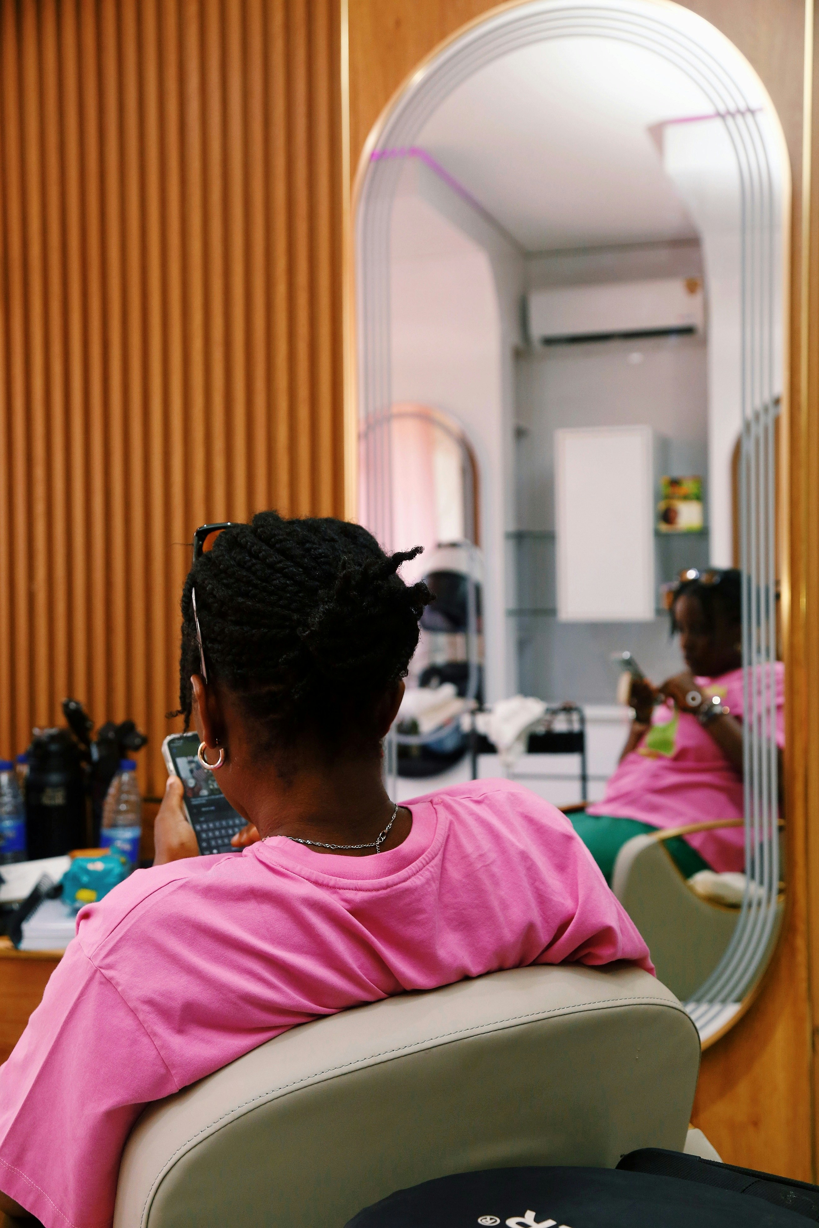 Woman in pink shirt looks at phone in salon.