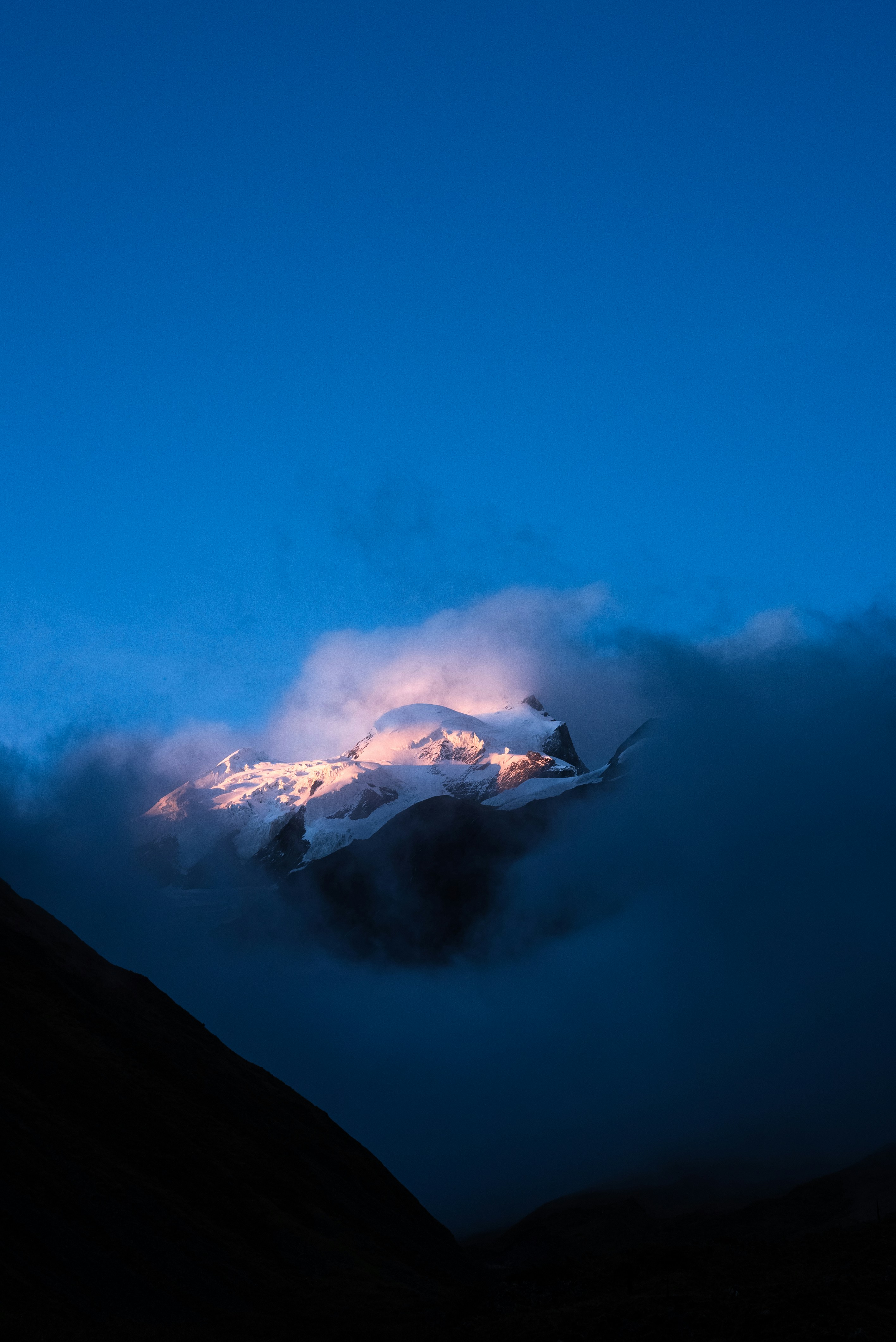 Berggipfel, der von Sonnenaufgang durch Wolken beleuchtet wird.