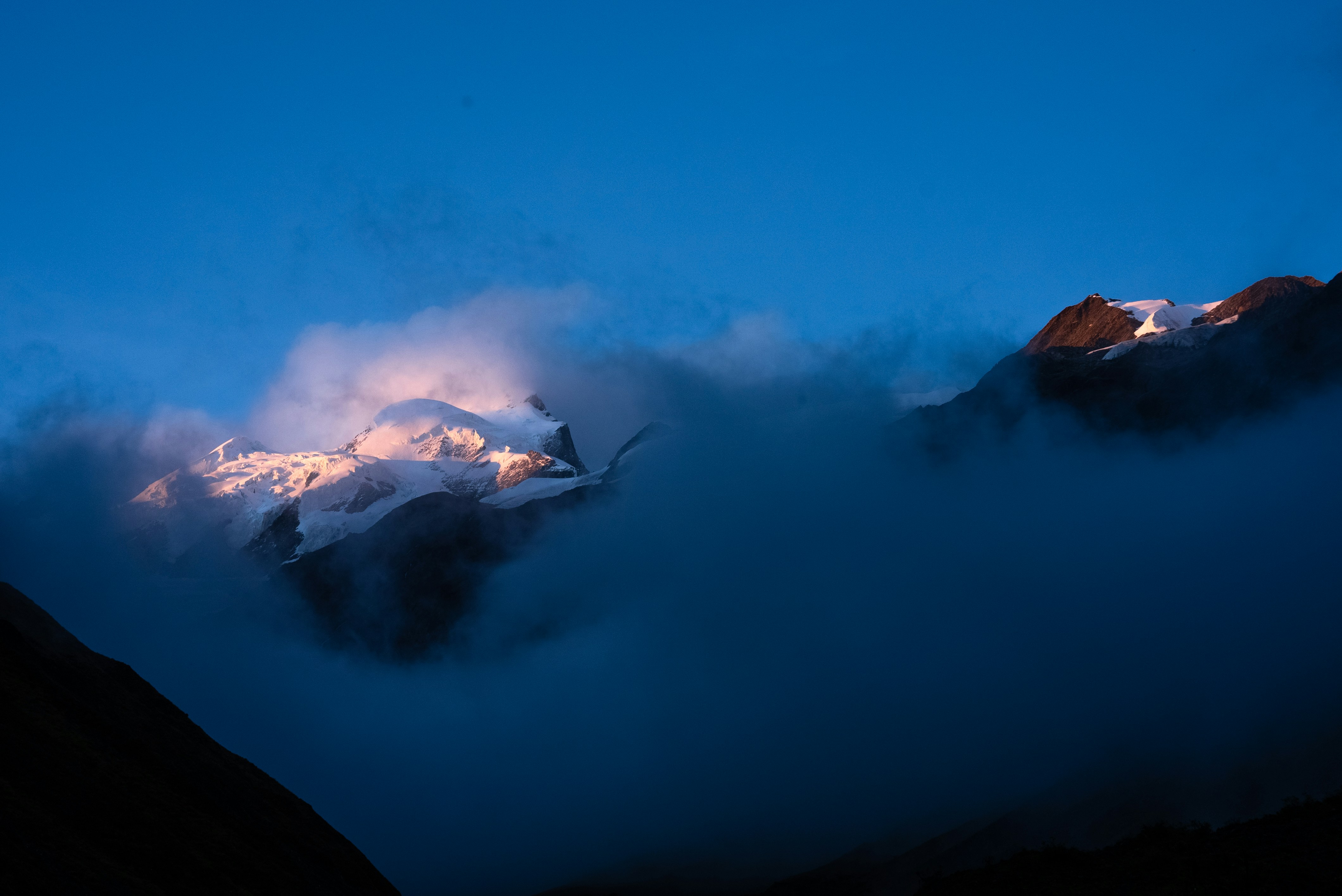 Verschneite Berggipfel, die von Sonnenaufgang durch Wolken beleuchtet werden.