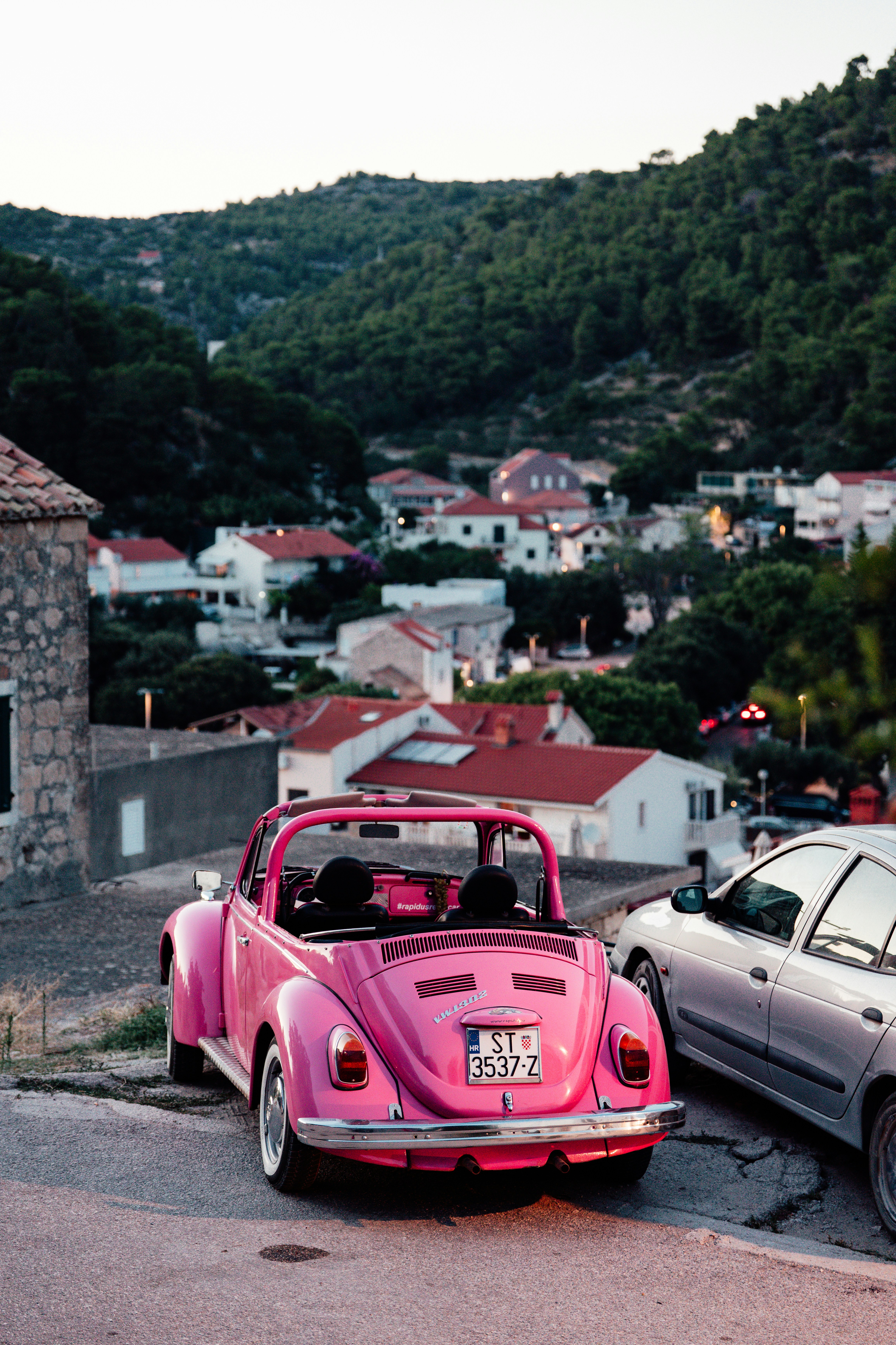 Pink convertible classic car parked in a village.