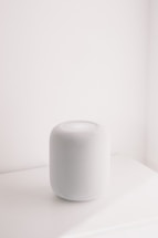 A white smart speaker on a white surface.