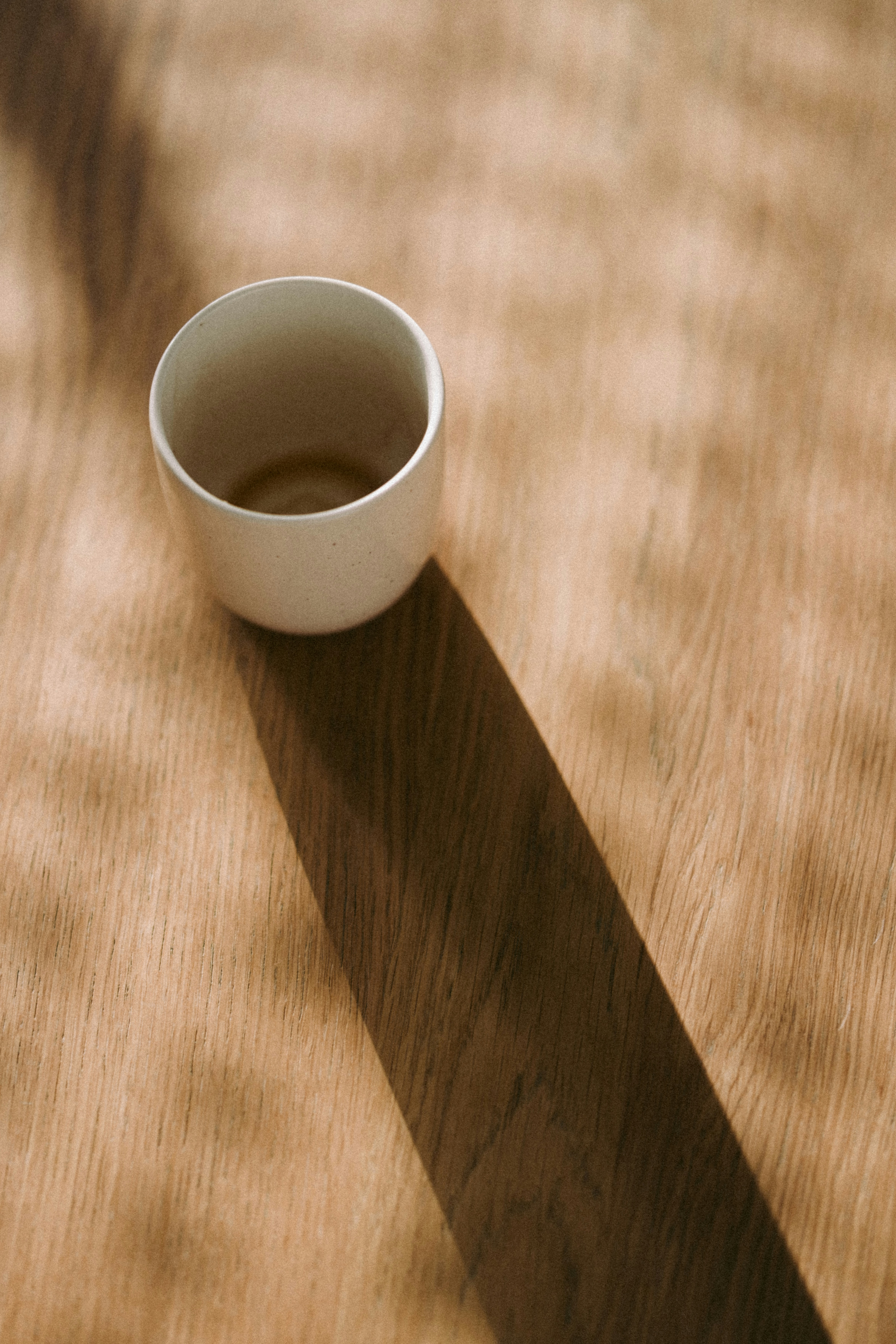 A white cup casting a shadow on a wooden surface