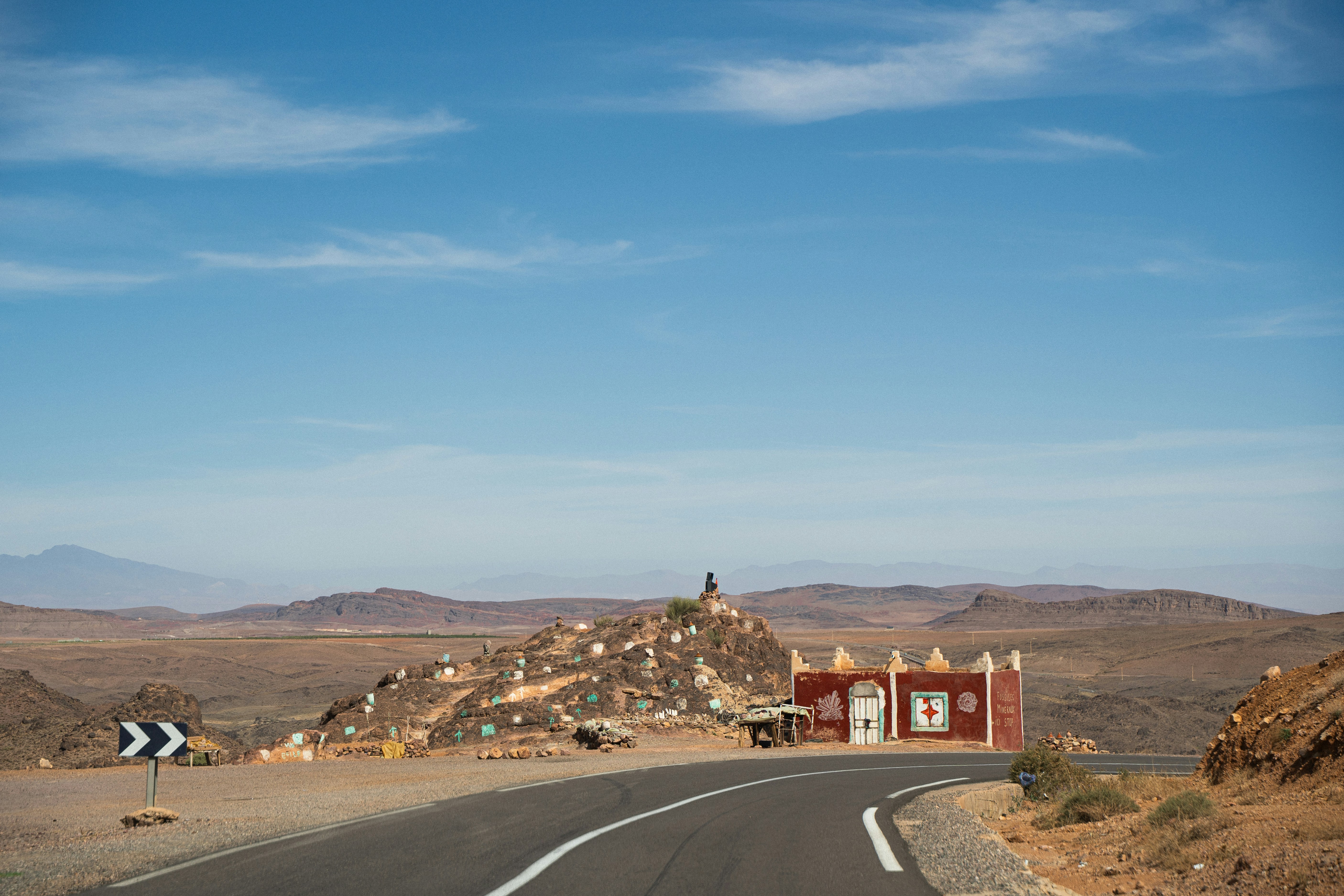 Red building on rocky hill beside desert road.