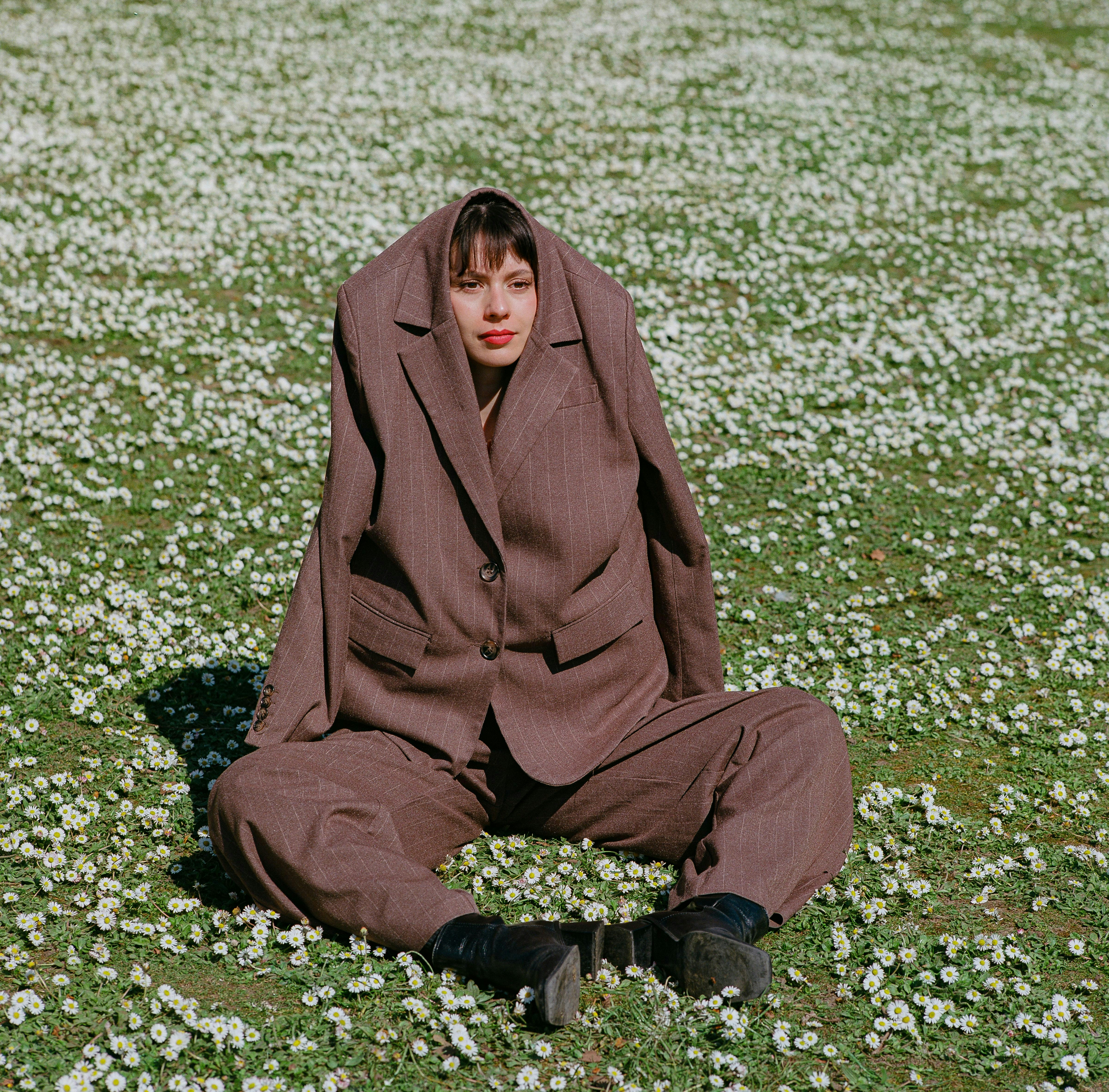 Çiçek tarlasında oversized takım elbiseyle oturan kişi - sürreal moda