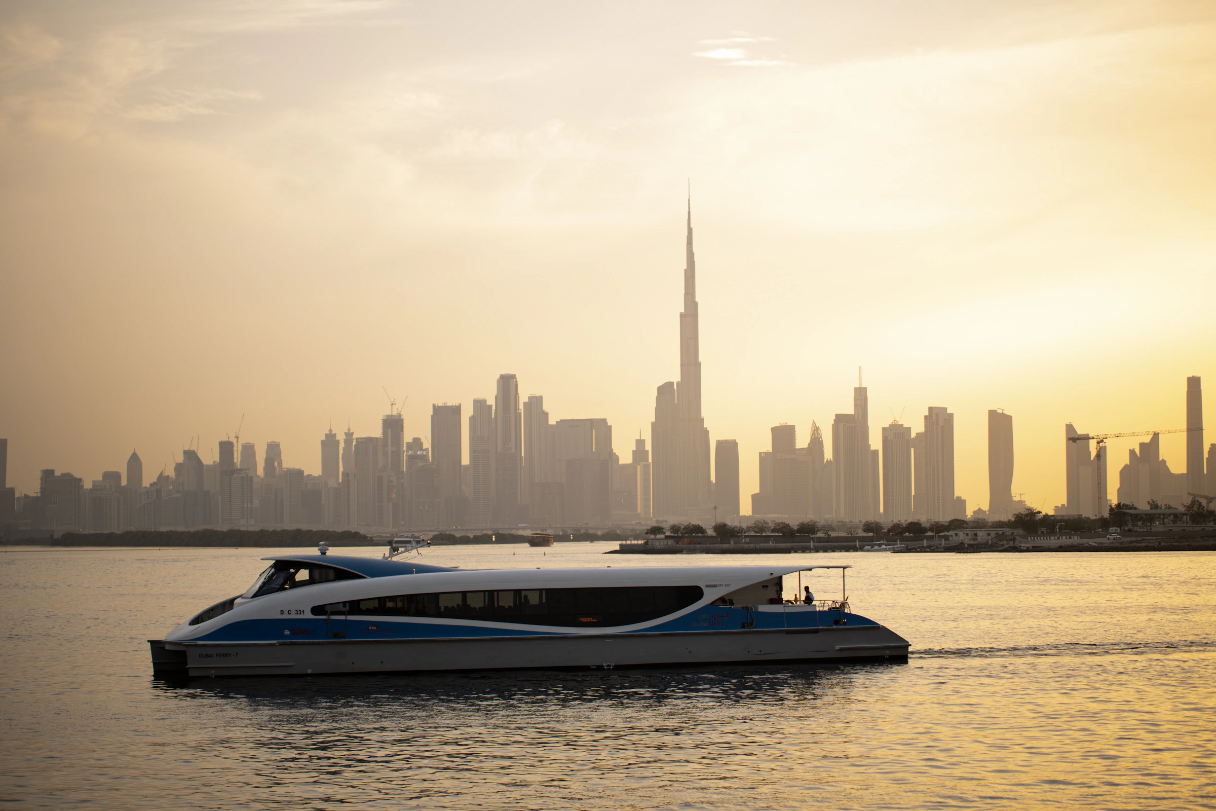 Luxury boat sailing past the illuminated Dubai skyline at sunset