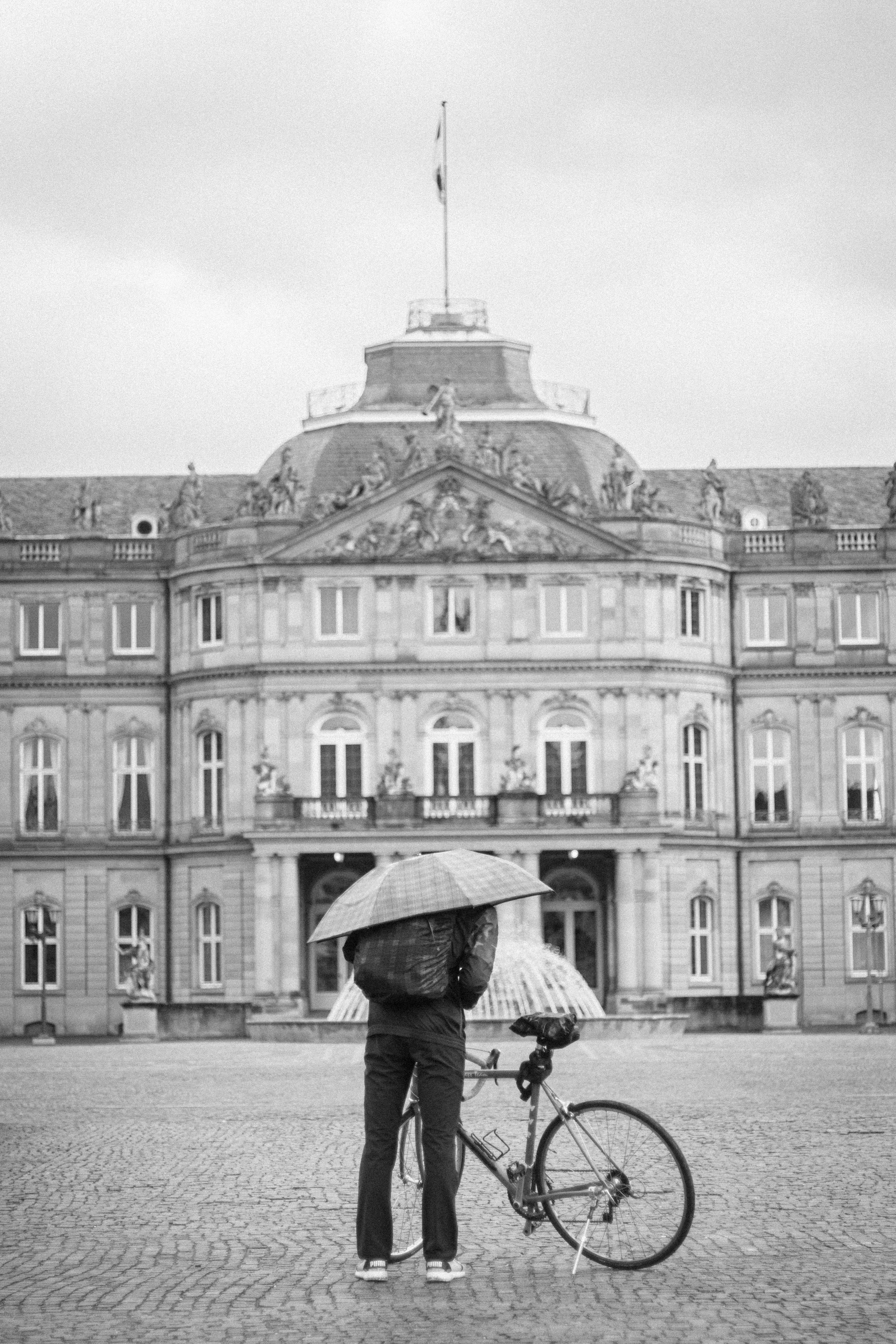 Person mit Regenschirm und Fahrrad vor dem Palast
