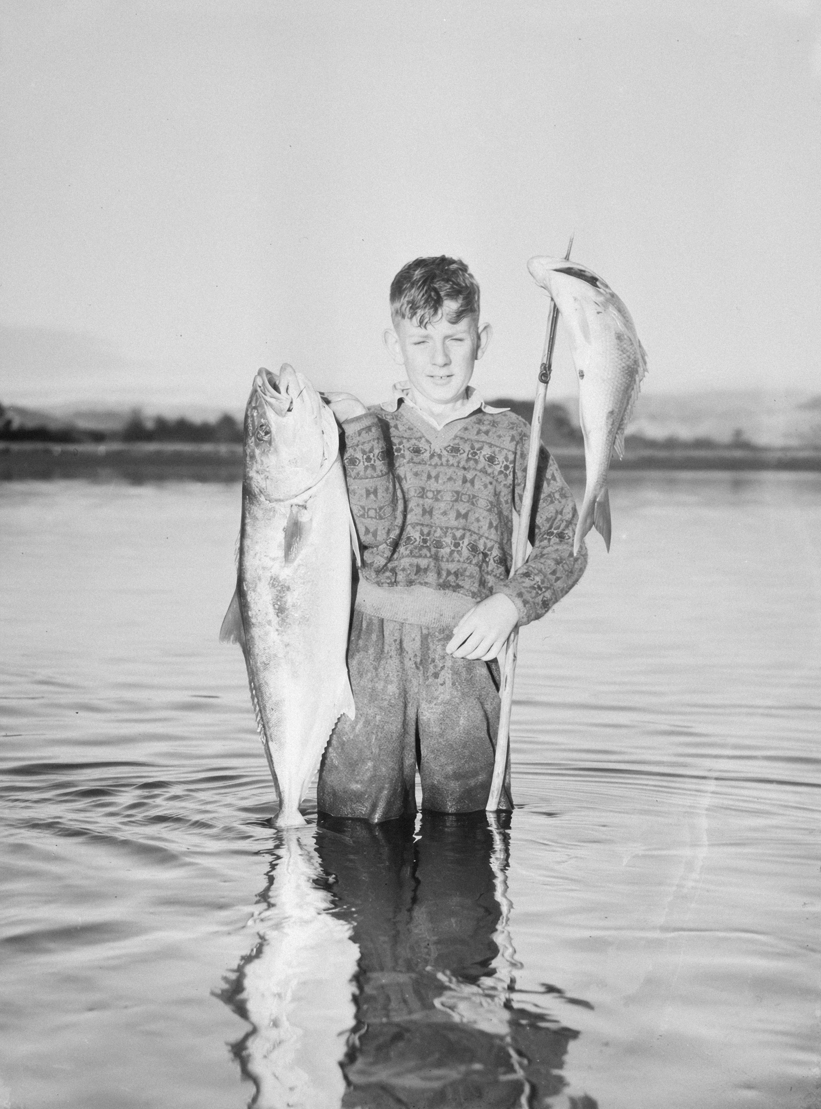 Young fisherman proudly displays two large fish.