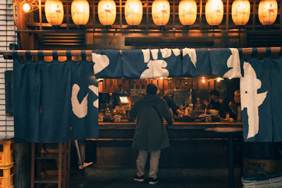 A person entering a dimly lit Japanese izakaya restaurant at night