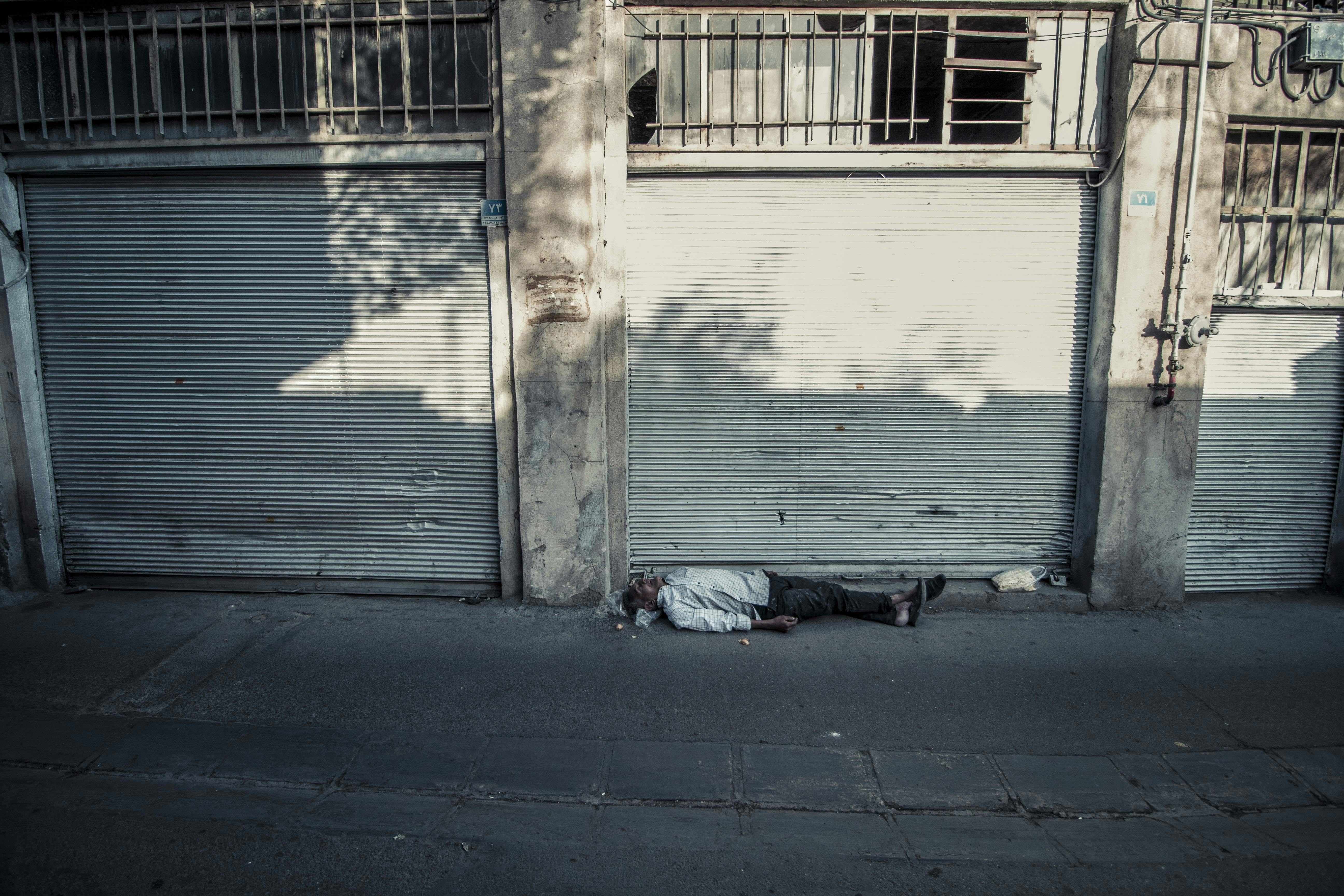 Man lying on the street in front of closed shops.
