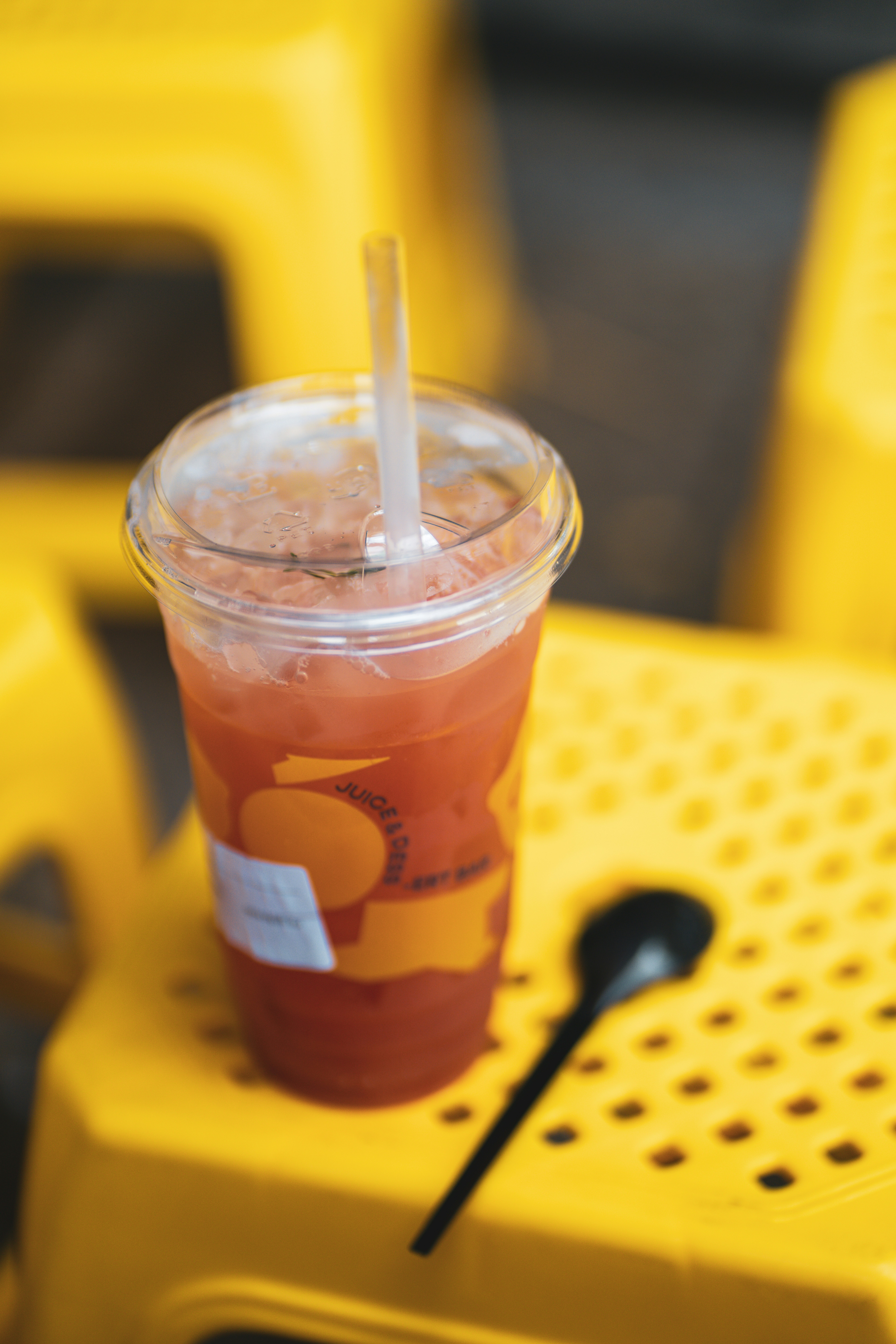 A refreshing pink drink with a straw on yellow chairs.