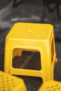 A bright yellow plastic stool on a dark surface.