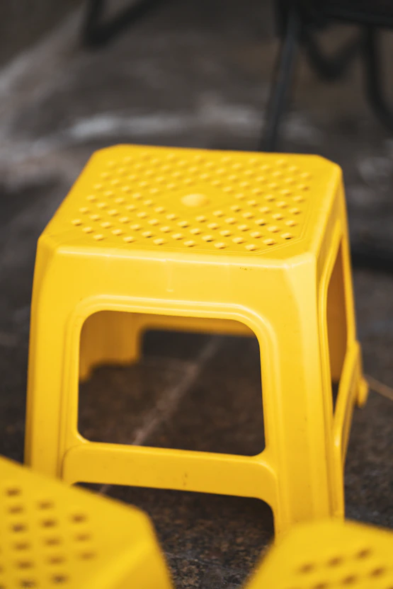 A bright yellow plastic stool on a dark surface.
