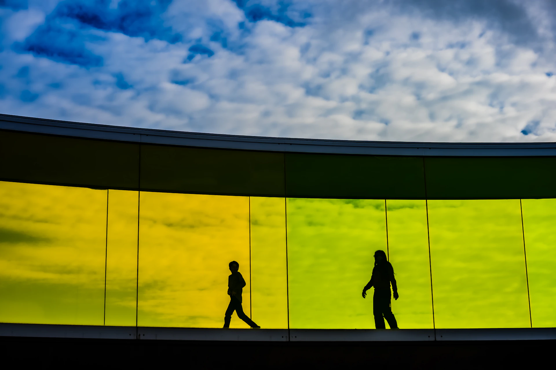 Silhouettes of two people walking on a colorful walkway.