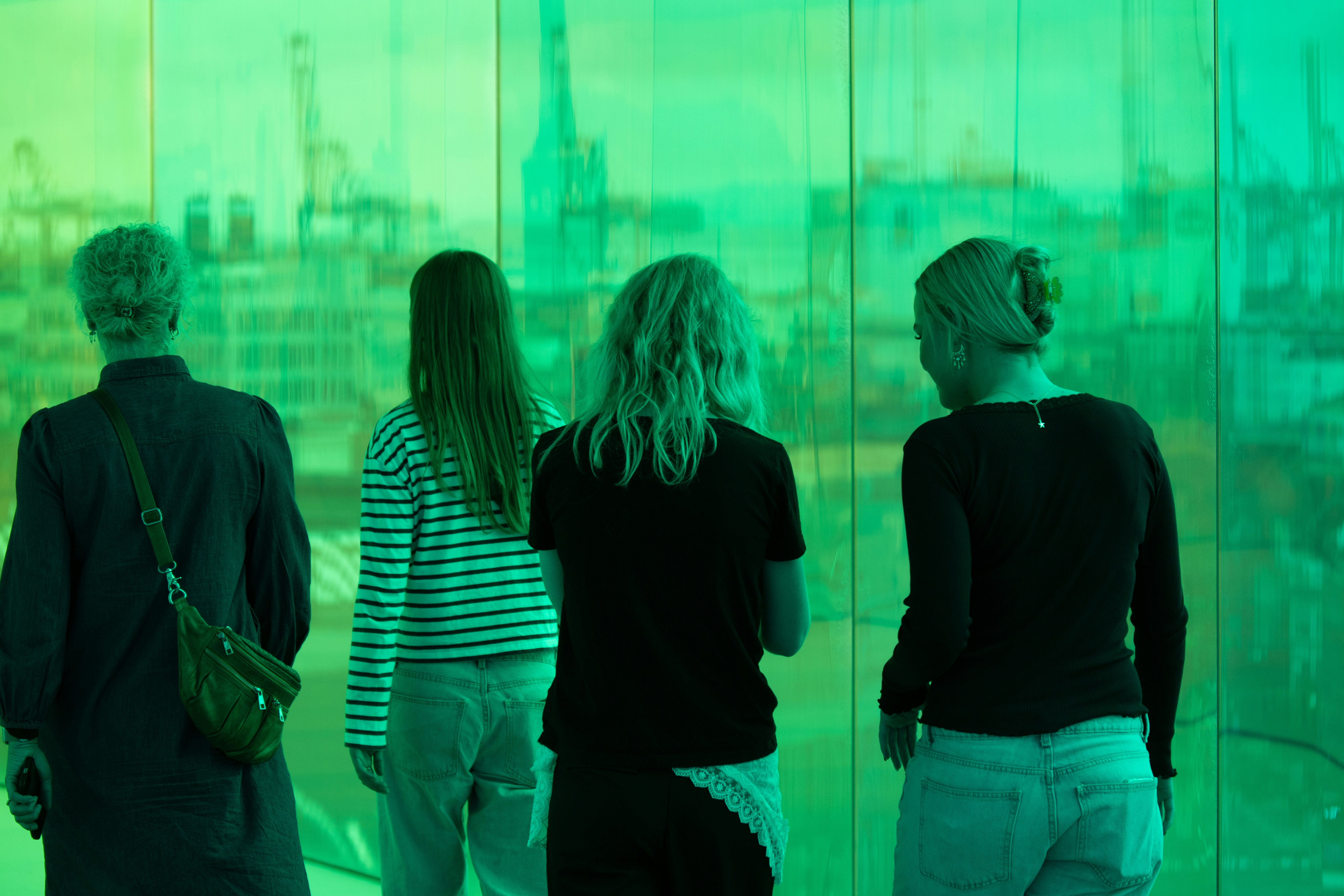 Four people look through a green-tinted window.