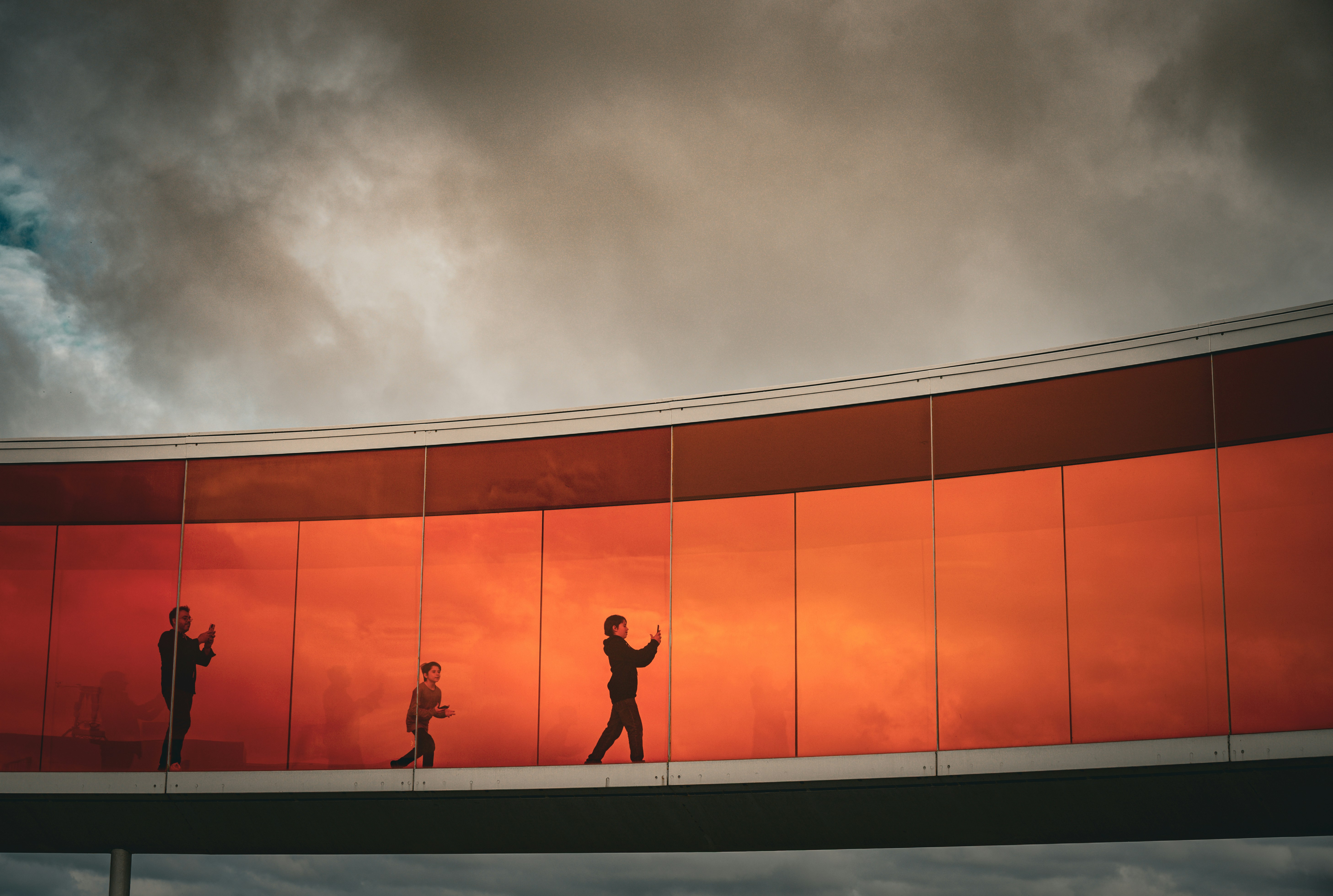 People walk on a colorful elevated walkway under cloudy skies.