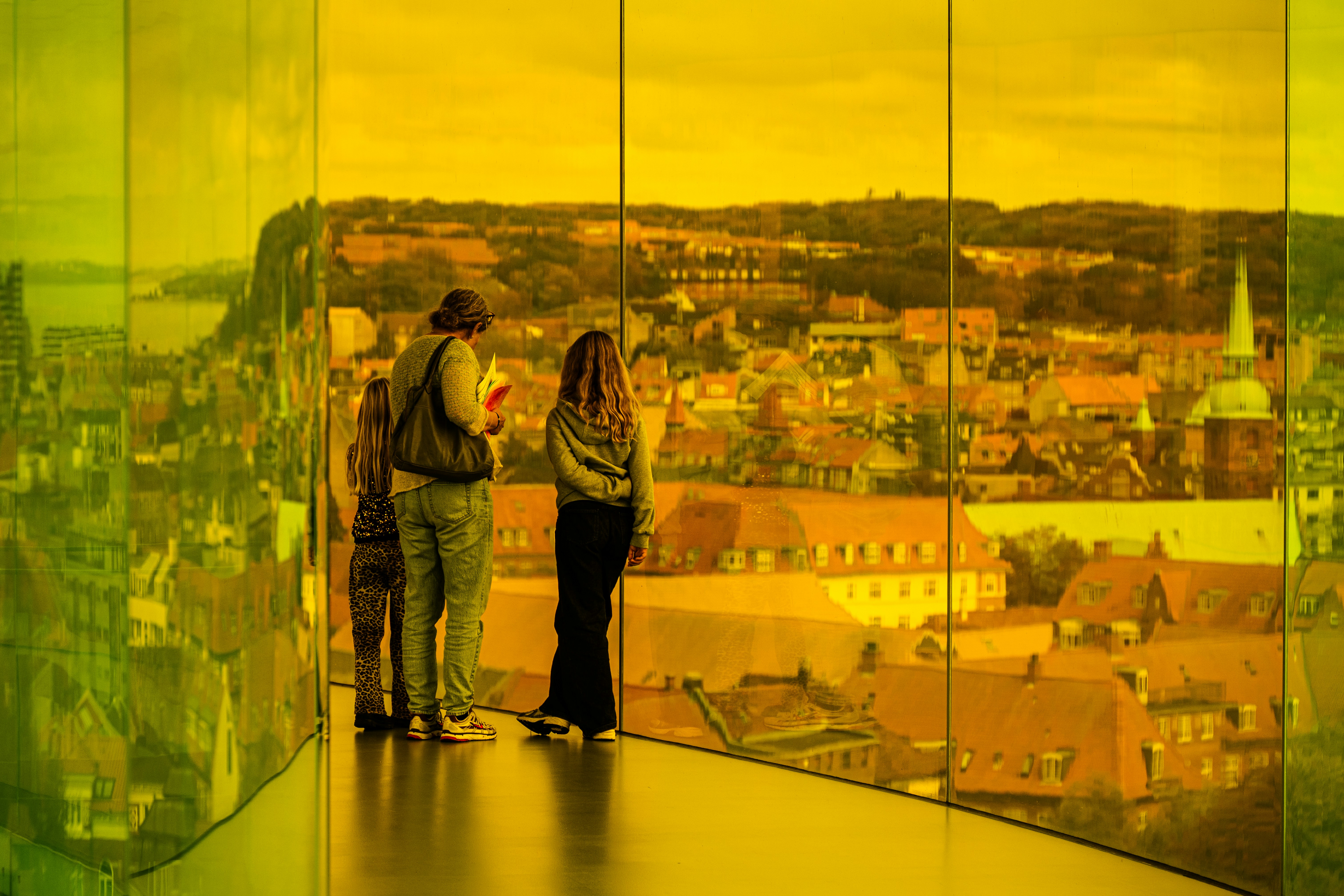 Two people view a city through a colored glass tunnel.
