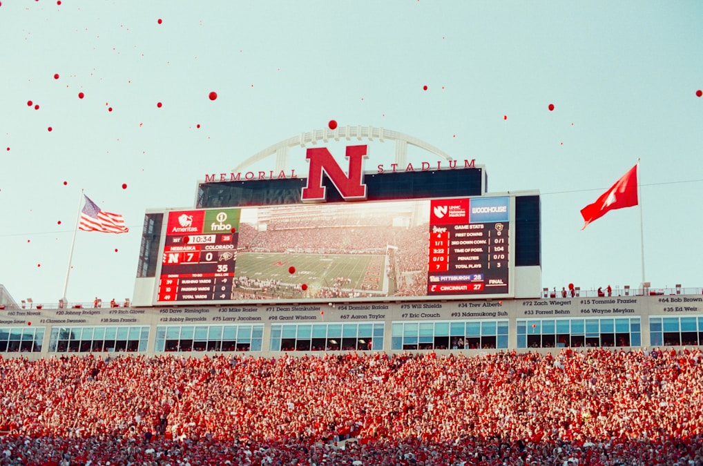 Fans celebrating at a college football stadium with scoreboards lit up
