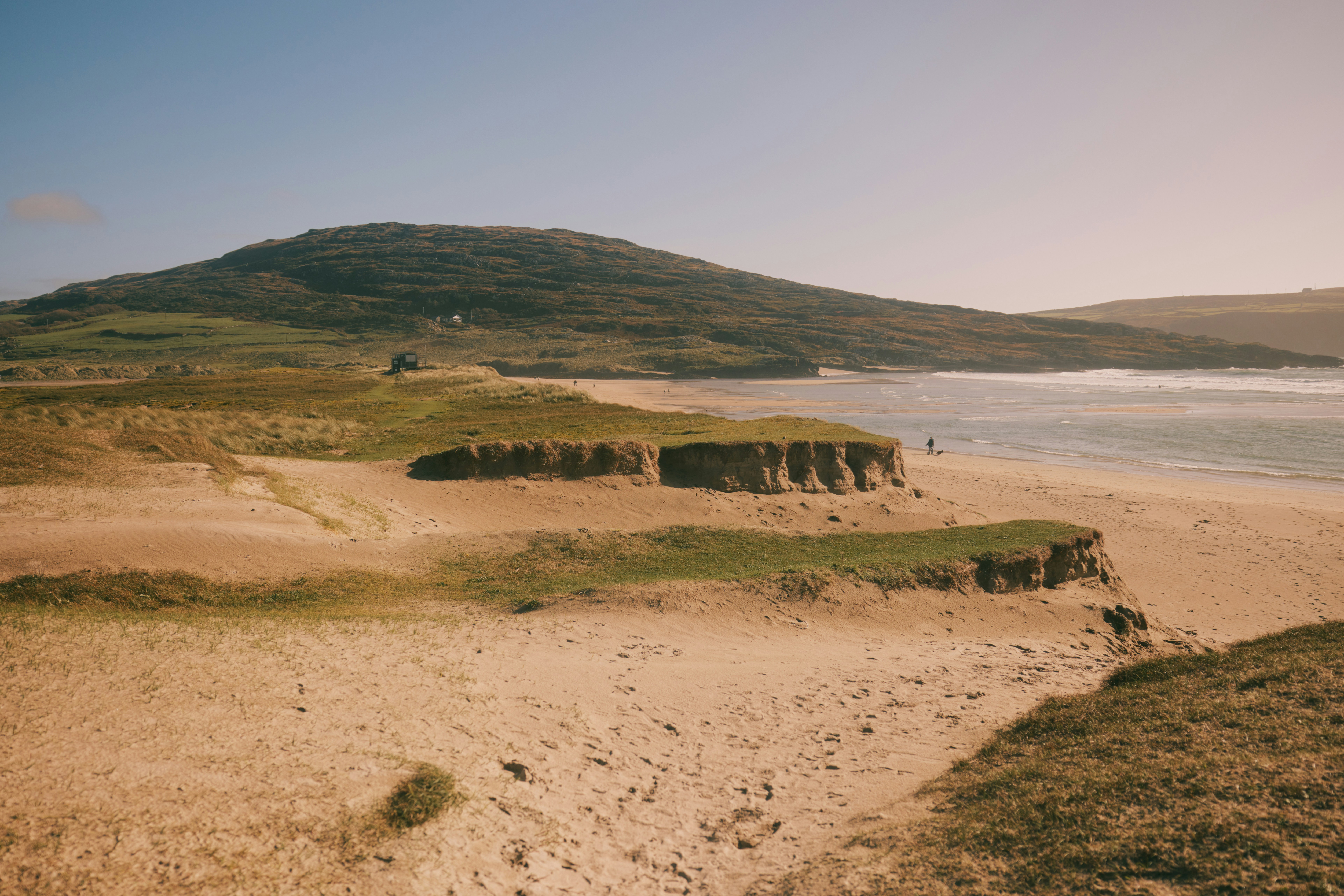 Sanddünen und grasbewachsene Hügel treffen auf das Meer