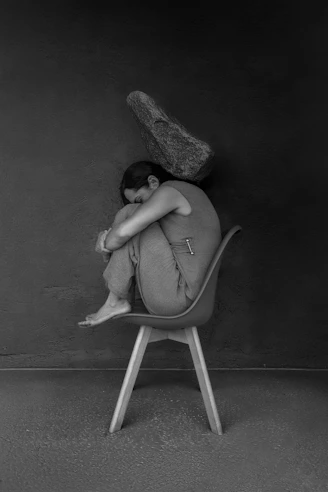 Woman curled up on chair with rock overhead