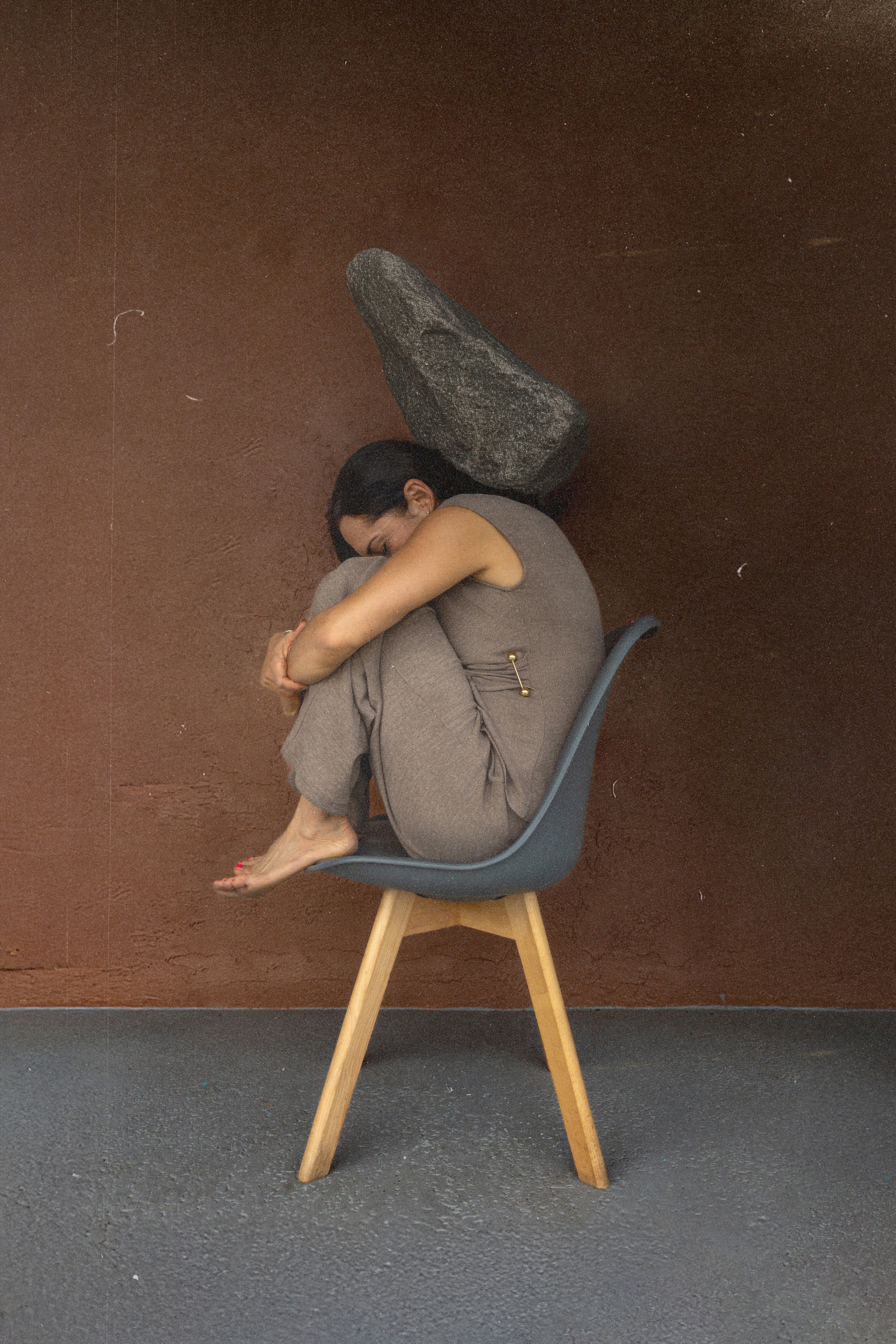 Woman curled on chair with rock overhead