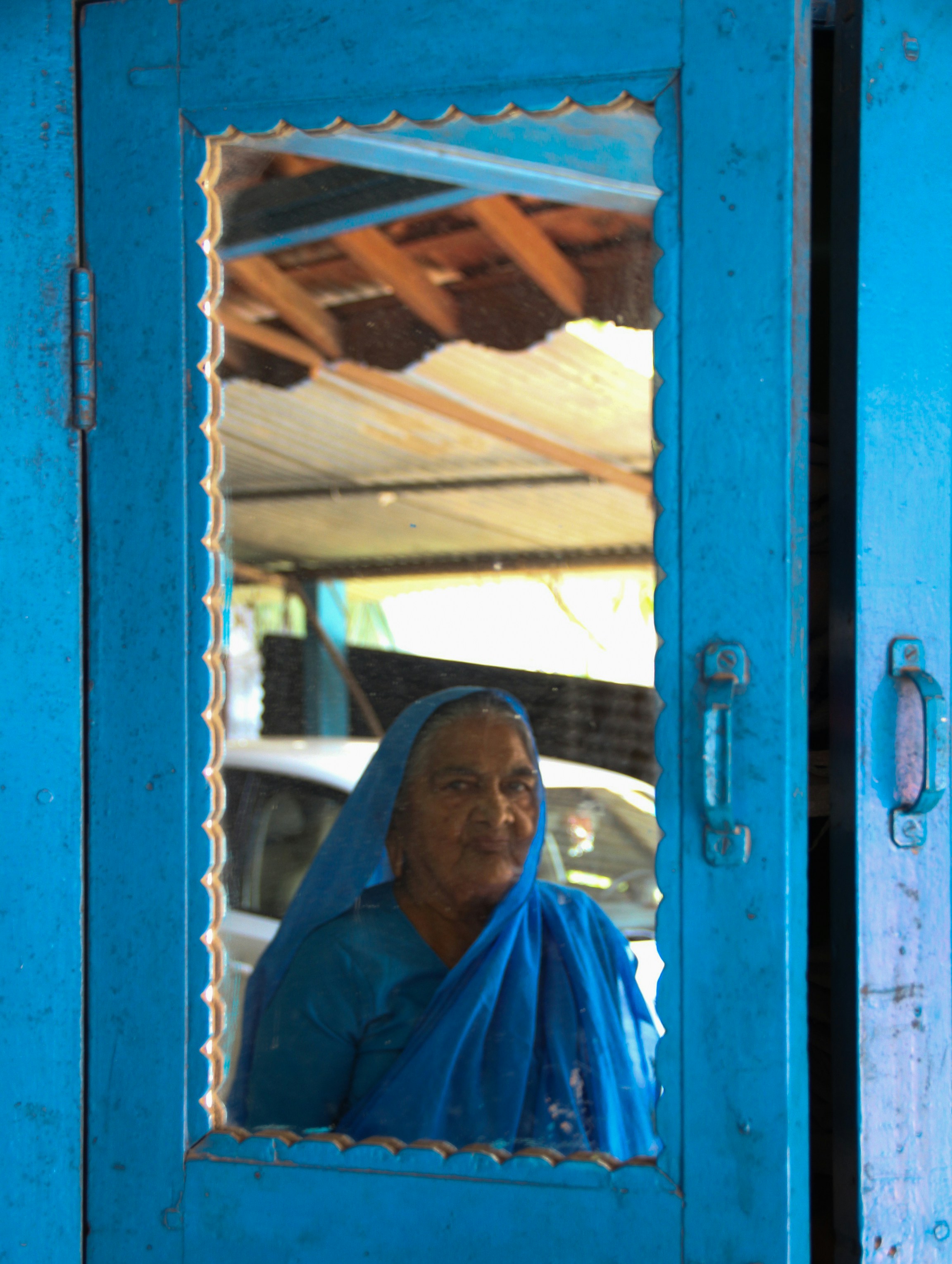 Elderly woman in blue sari looking through window