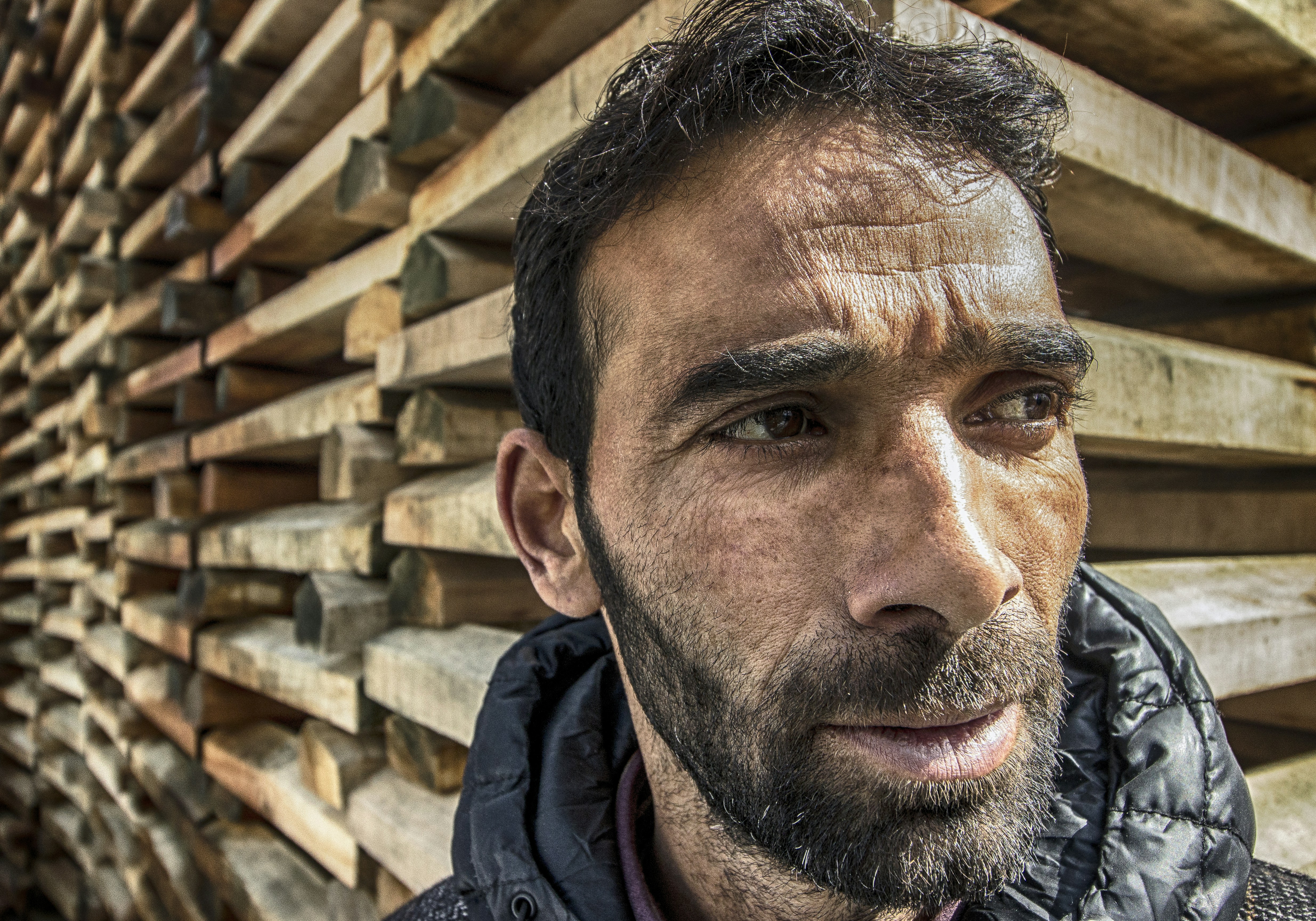 Man with beard standing by stacked lumber