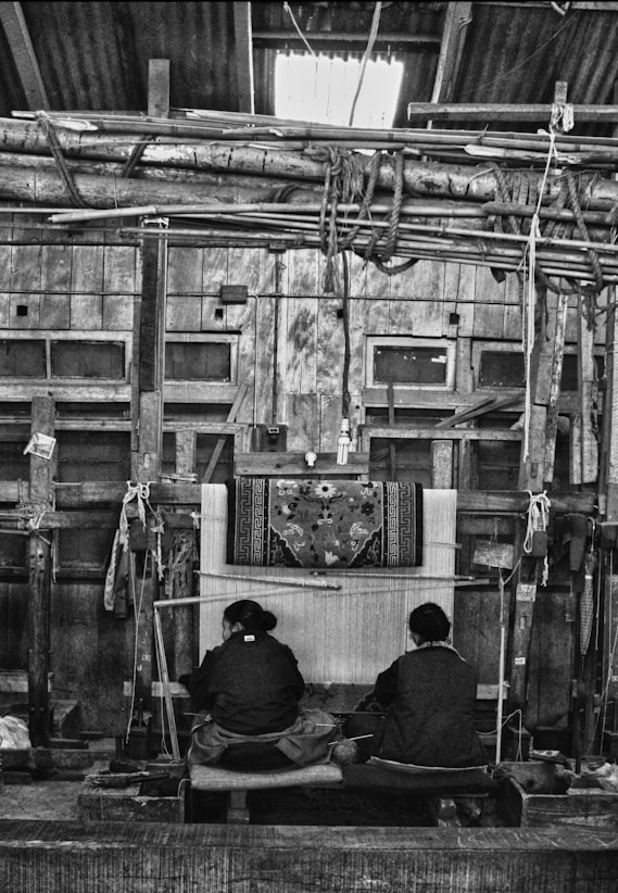 Two people weaving a rug on a loom