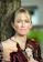 Blonde woman with blue eyes leaning against tree