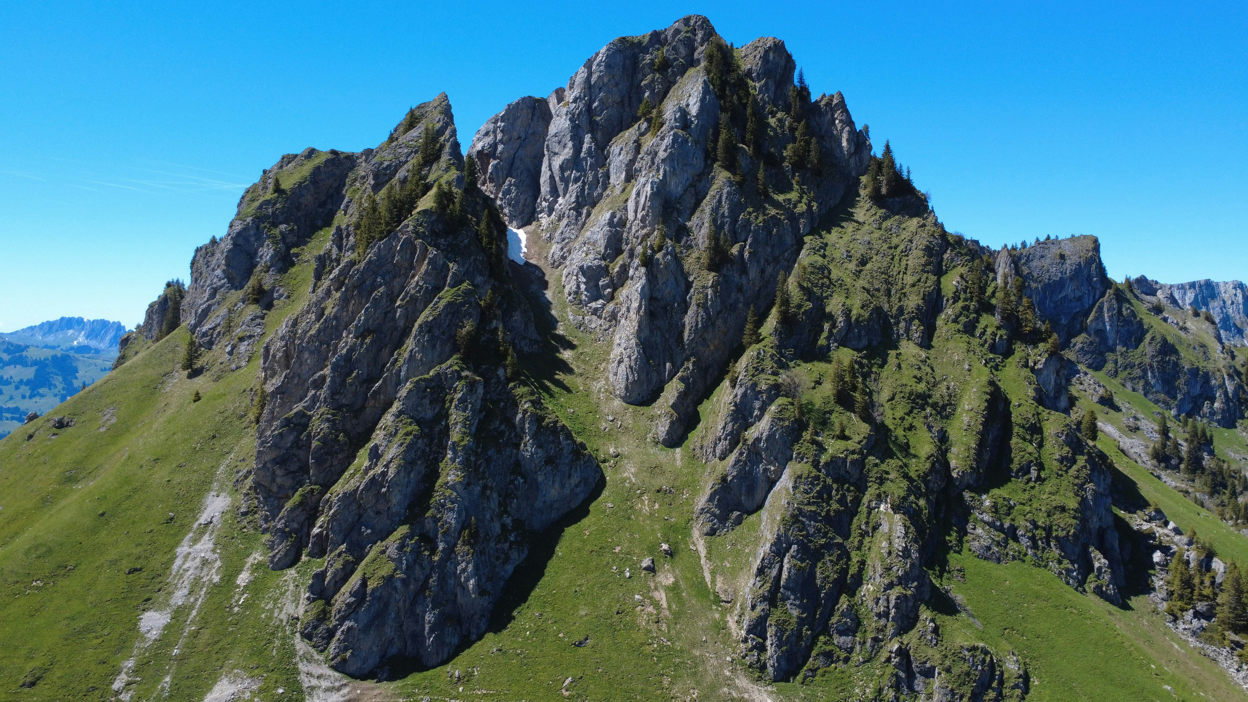 Jagged rocky mountain peak with green grassy slopes.