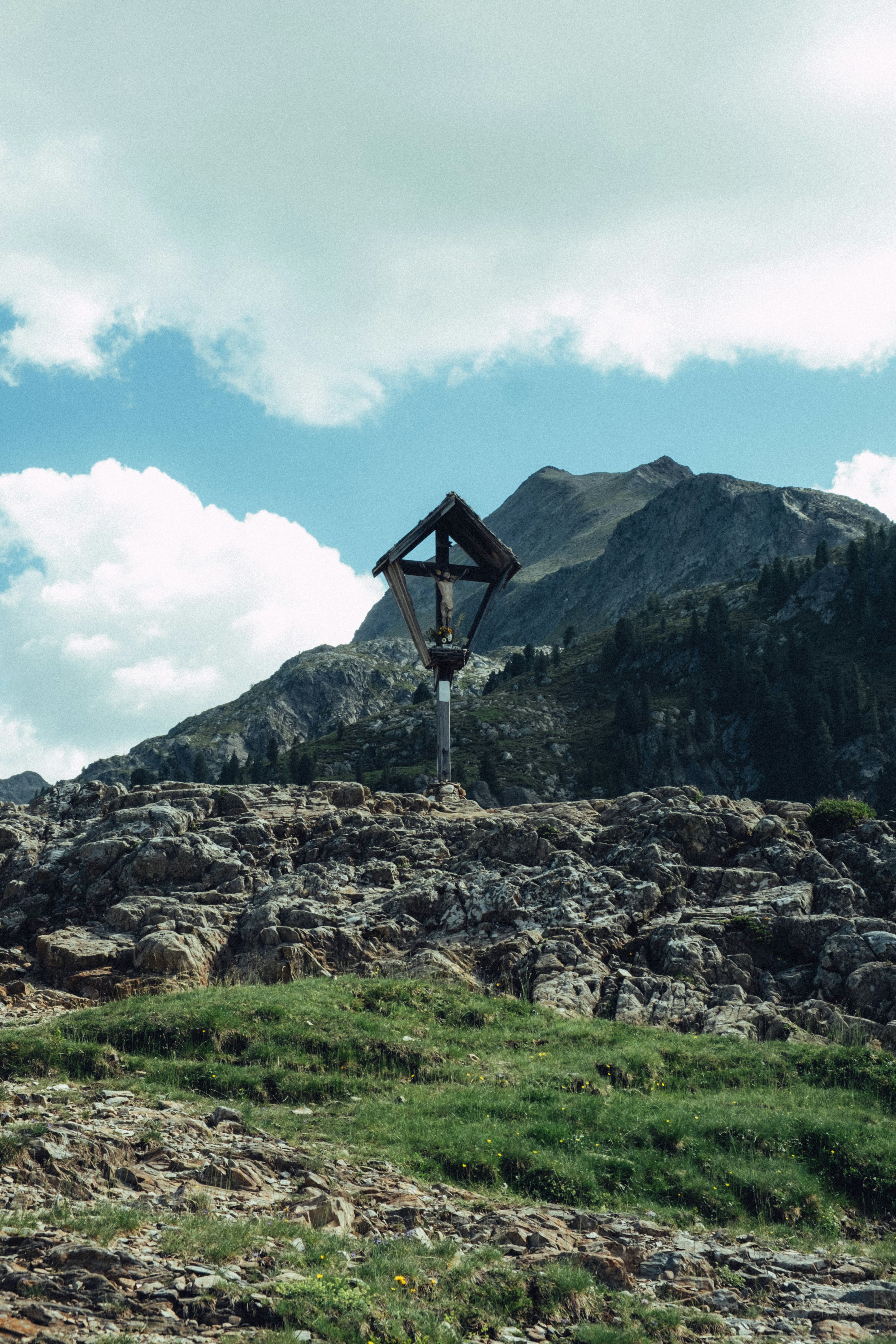 Wooden cross on rocky mountain peak under cloudy sky