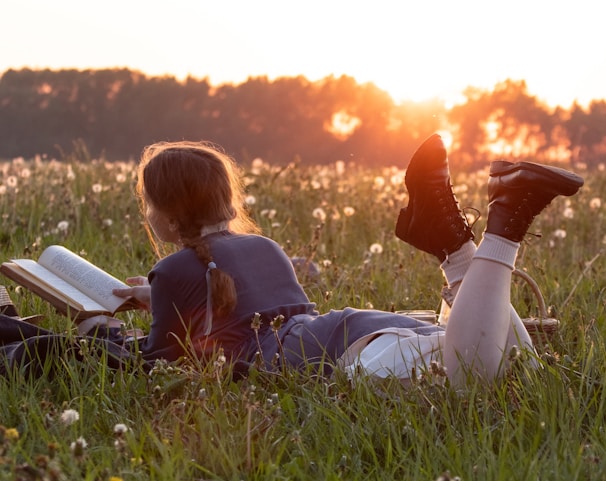 Young woman reading a book in a field at sunset