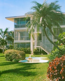 Tropical apartment building with a fountain and palm trees.