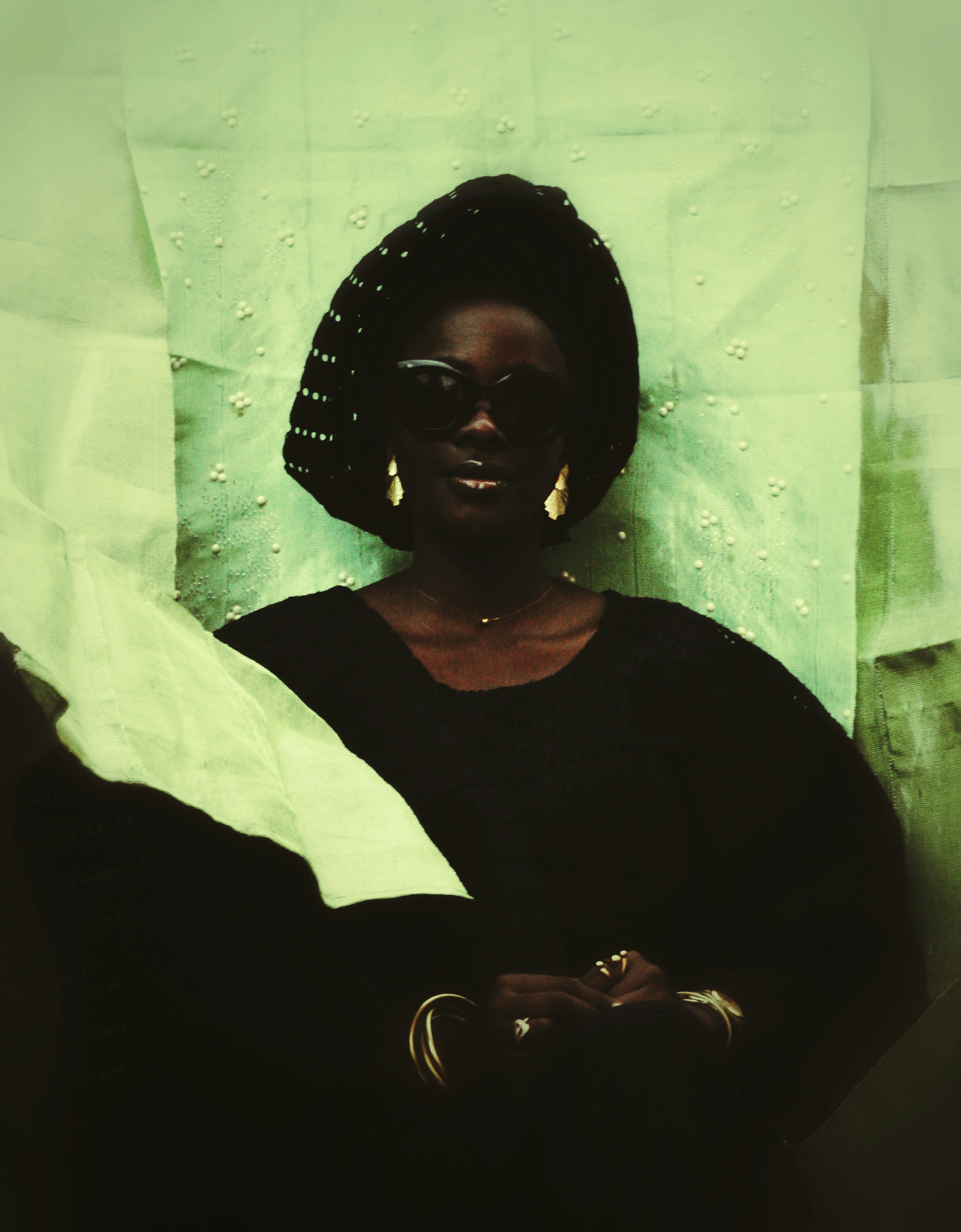 Woman wearing patterned headwrap and gold jewelry posing confidently.
