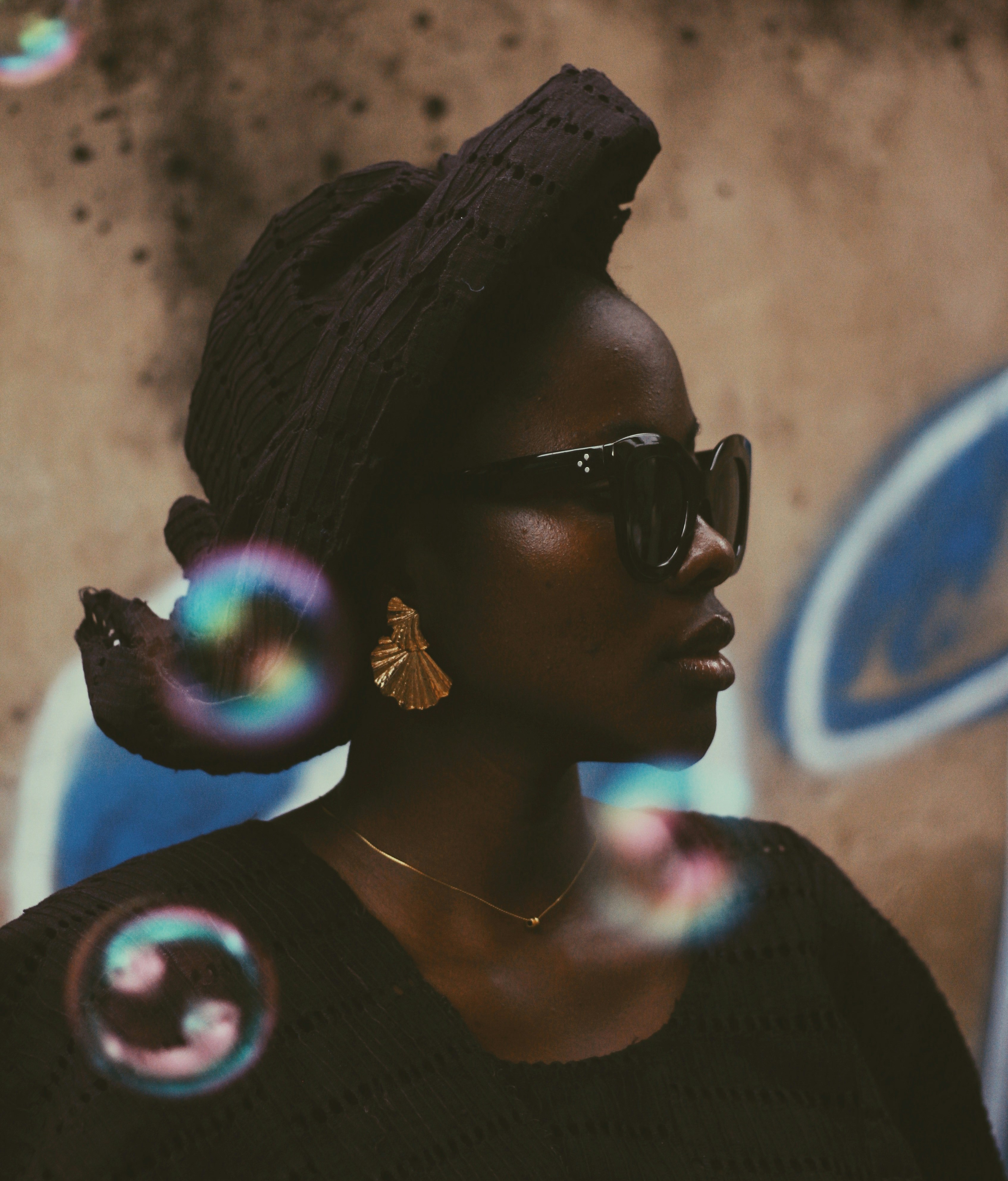 Woman wearing sunglasses and headwrap, bubbles floating.
