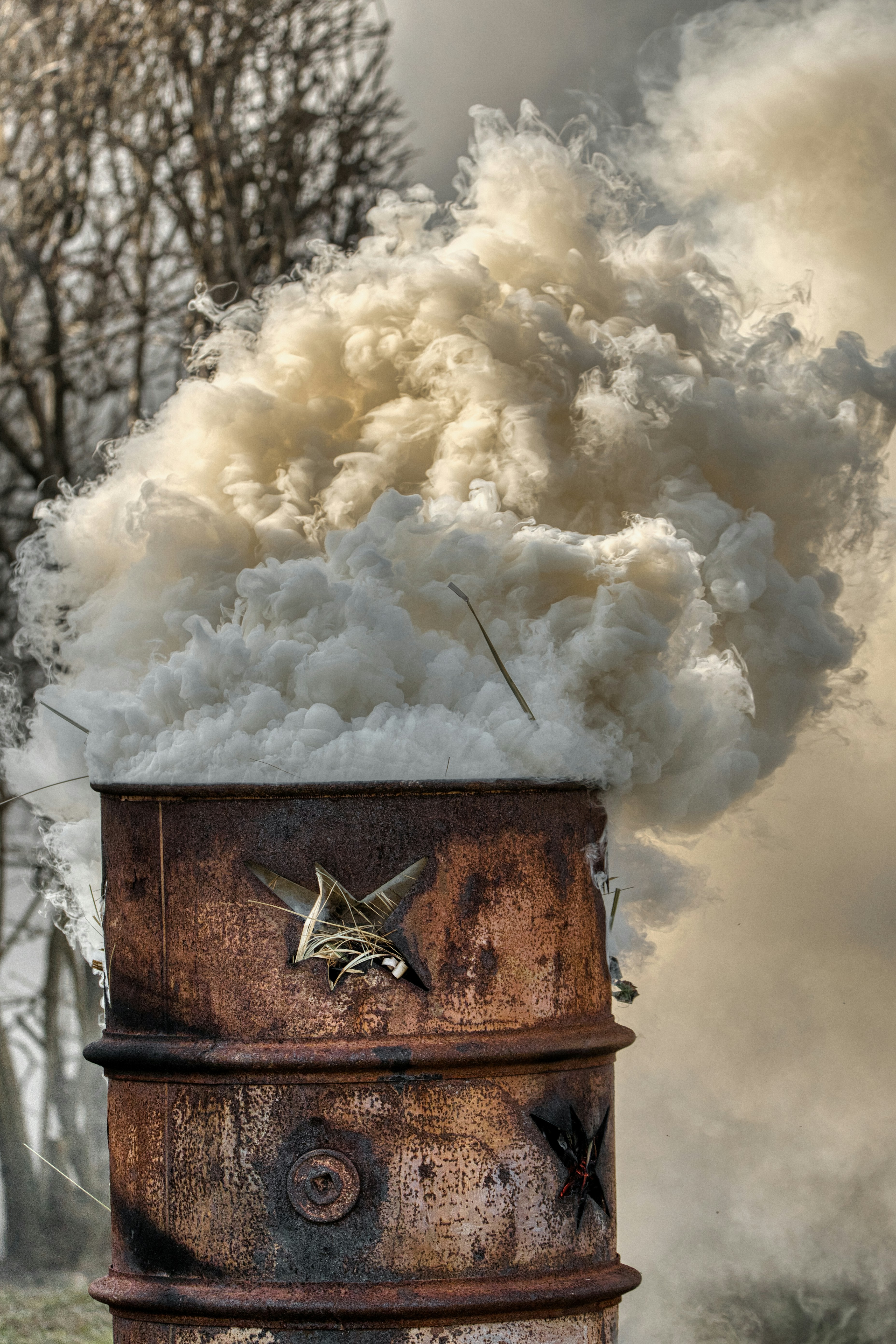 Thick white smoke billows from a rusty barrel.
